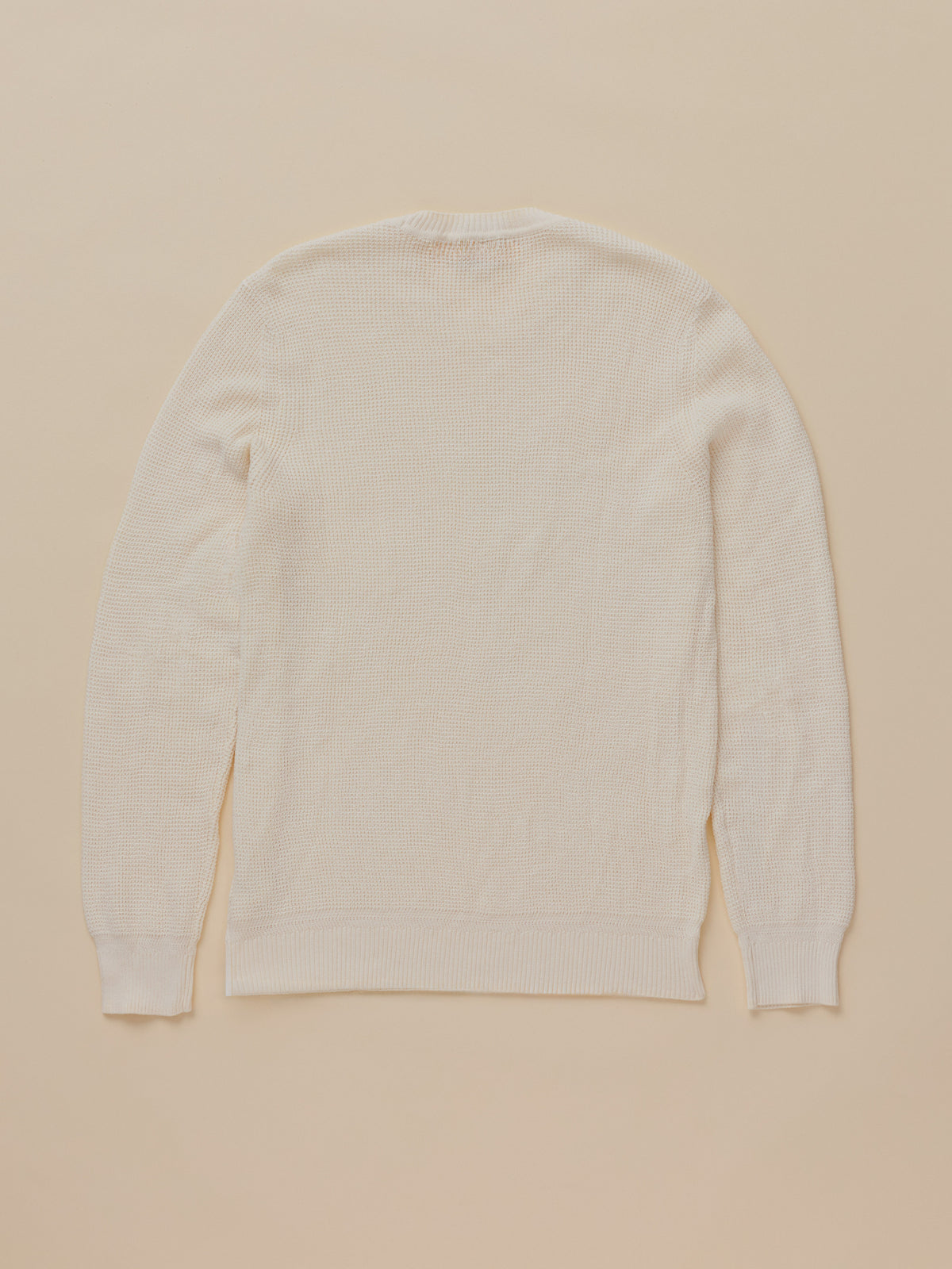 A cream-colored long-sleeve knit sweater shown from the back, laid flat on a solid beige background., image 7 of 7