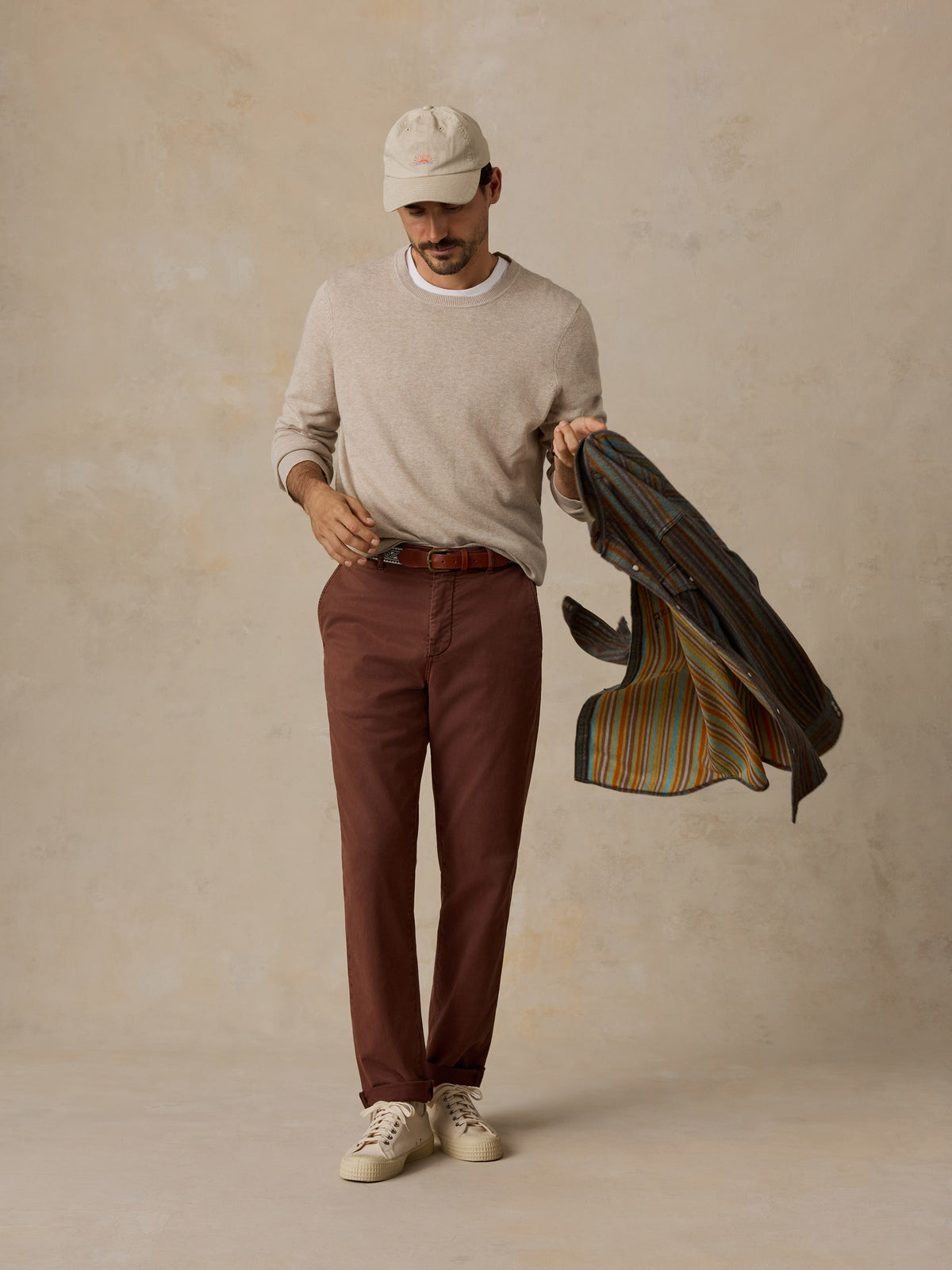 Man wearing a light beige sweater, brown trousers, a beige cap, and white sneakers.