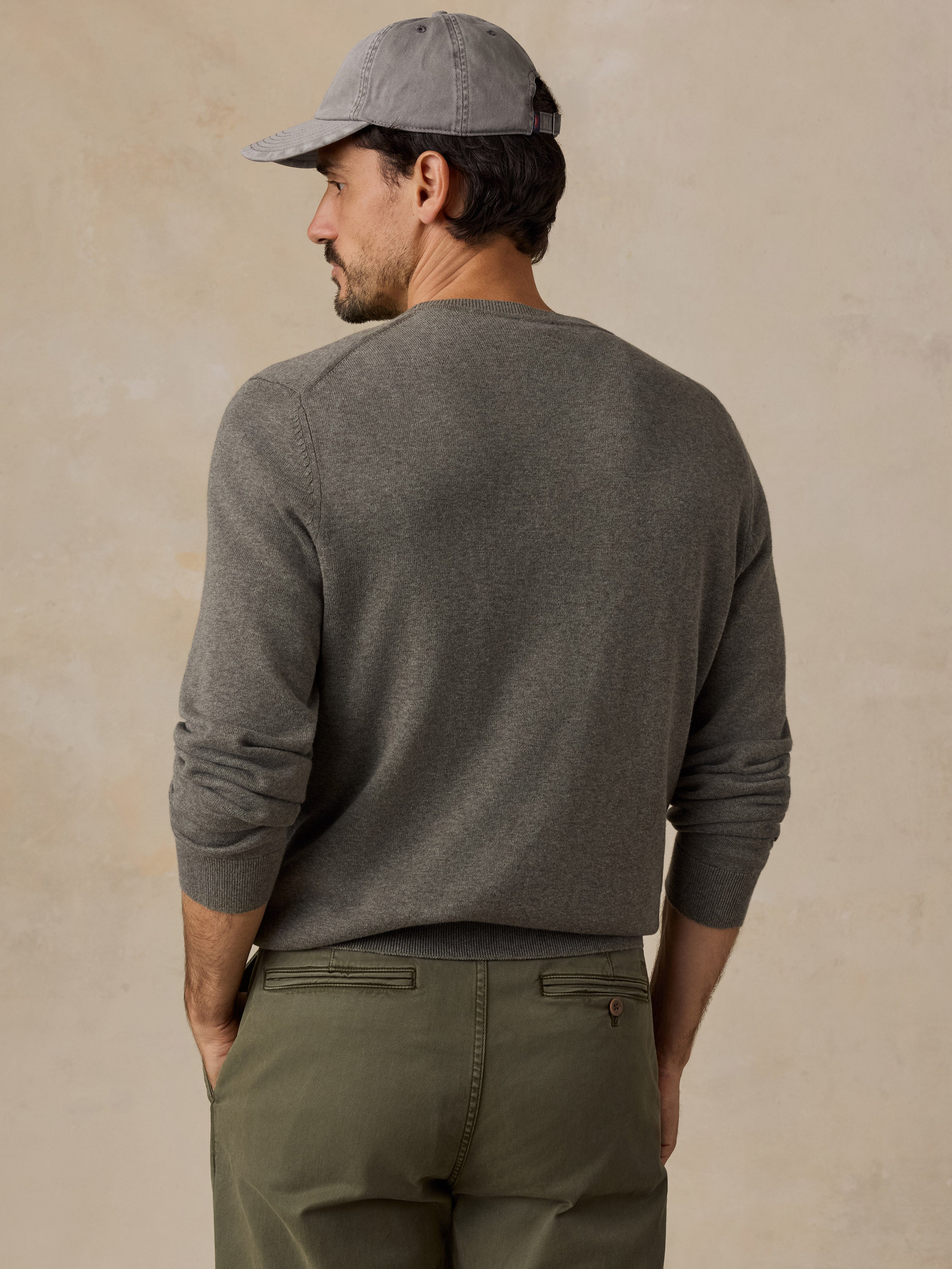 A man wearing a green long-sleeve knit sweater, olive green pants, and a gray baseball cap.