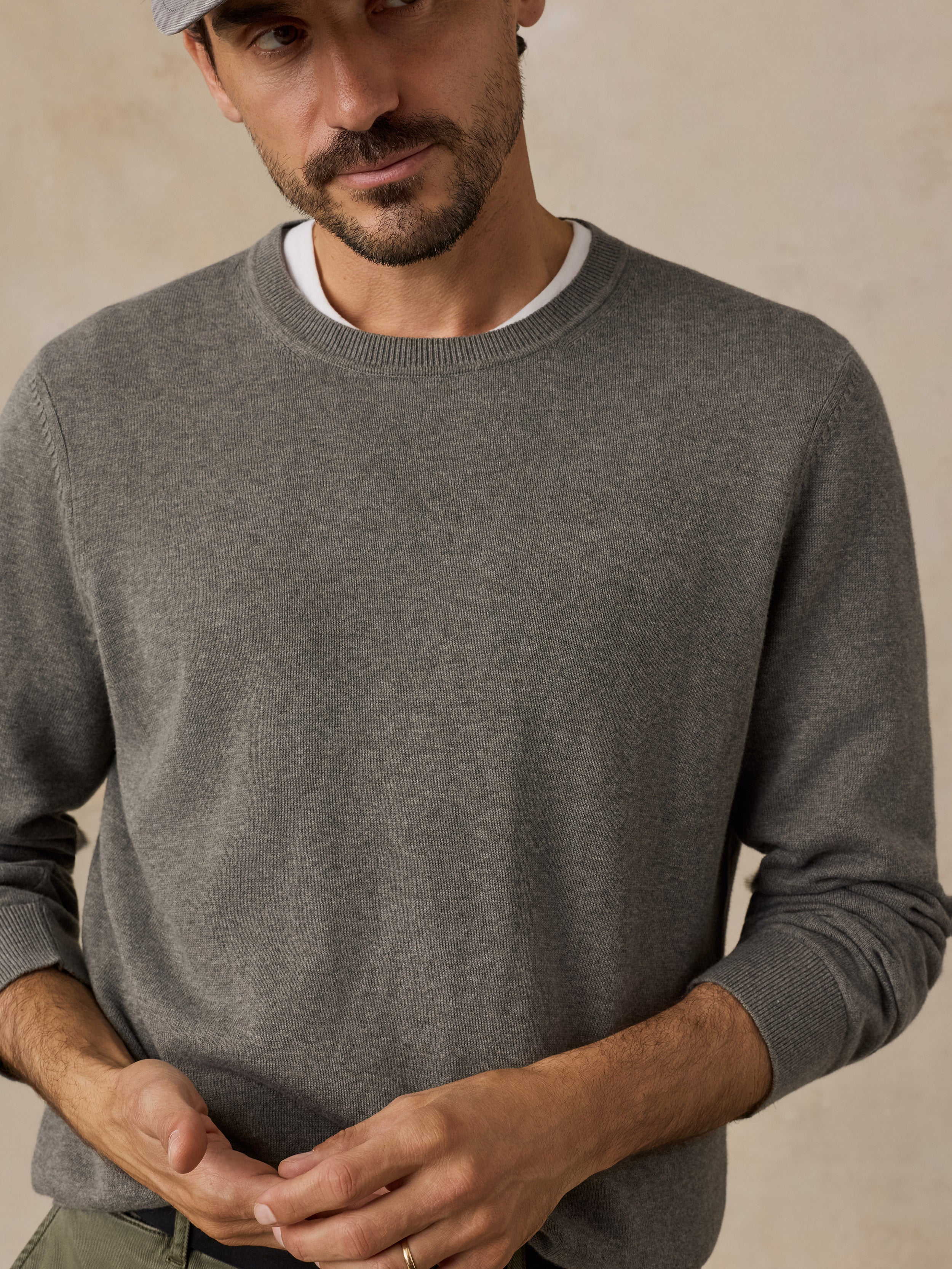 A man wearing a green crewneck sweater over a white undershirt.