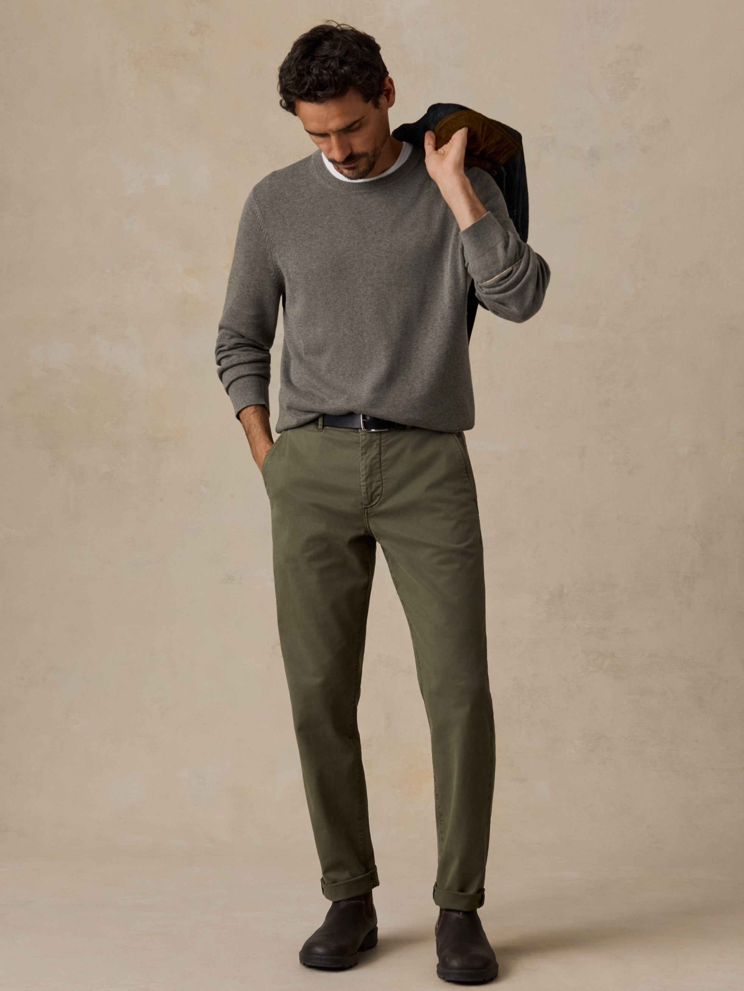 A man wearing a green long-sleeve knit sweater, olive green trousers, and dark brown shoes.