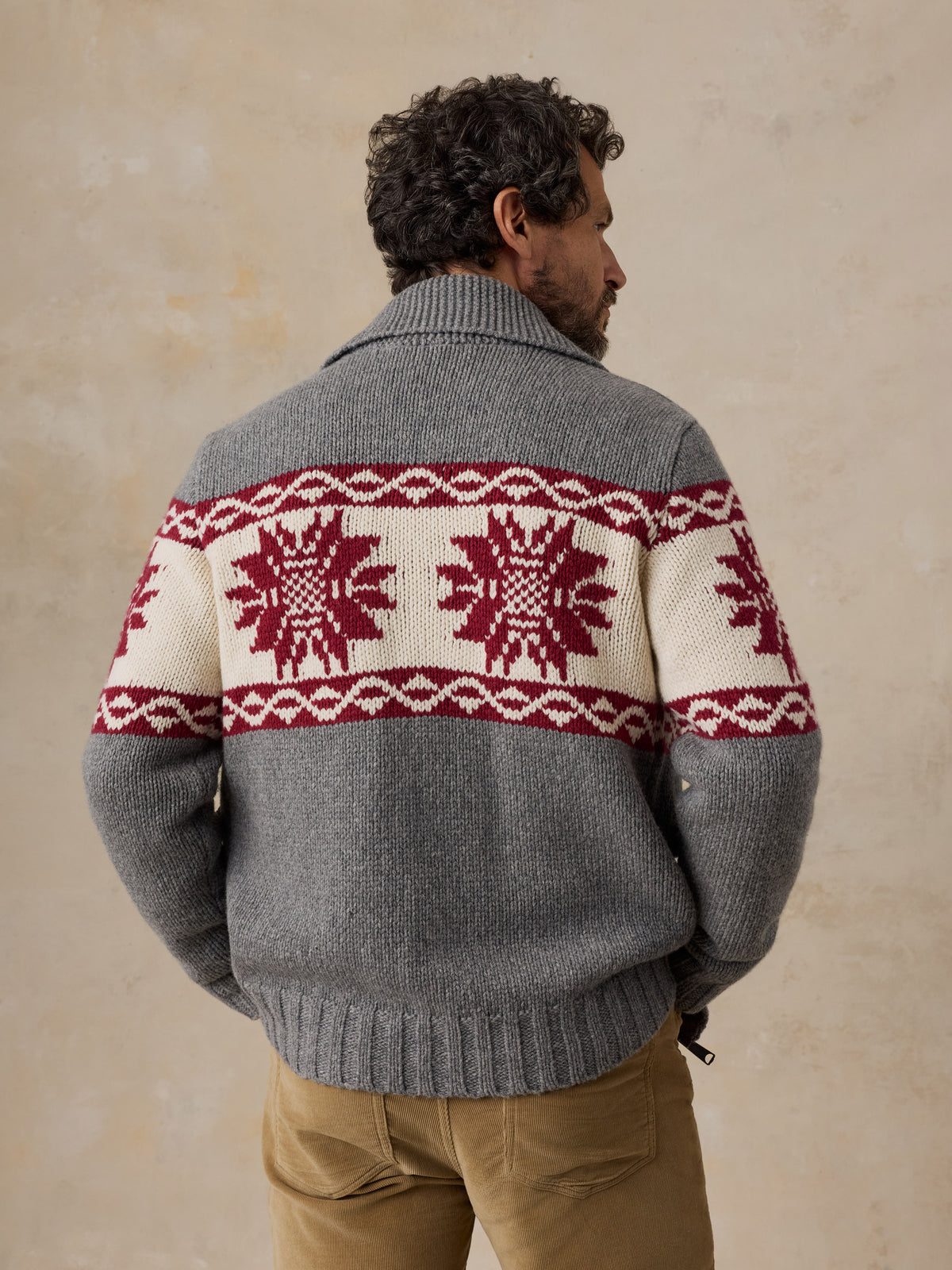 A man viewed from behind wearing a printed wool cardigan and tan pants, image 4 of 5