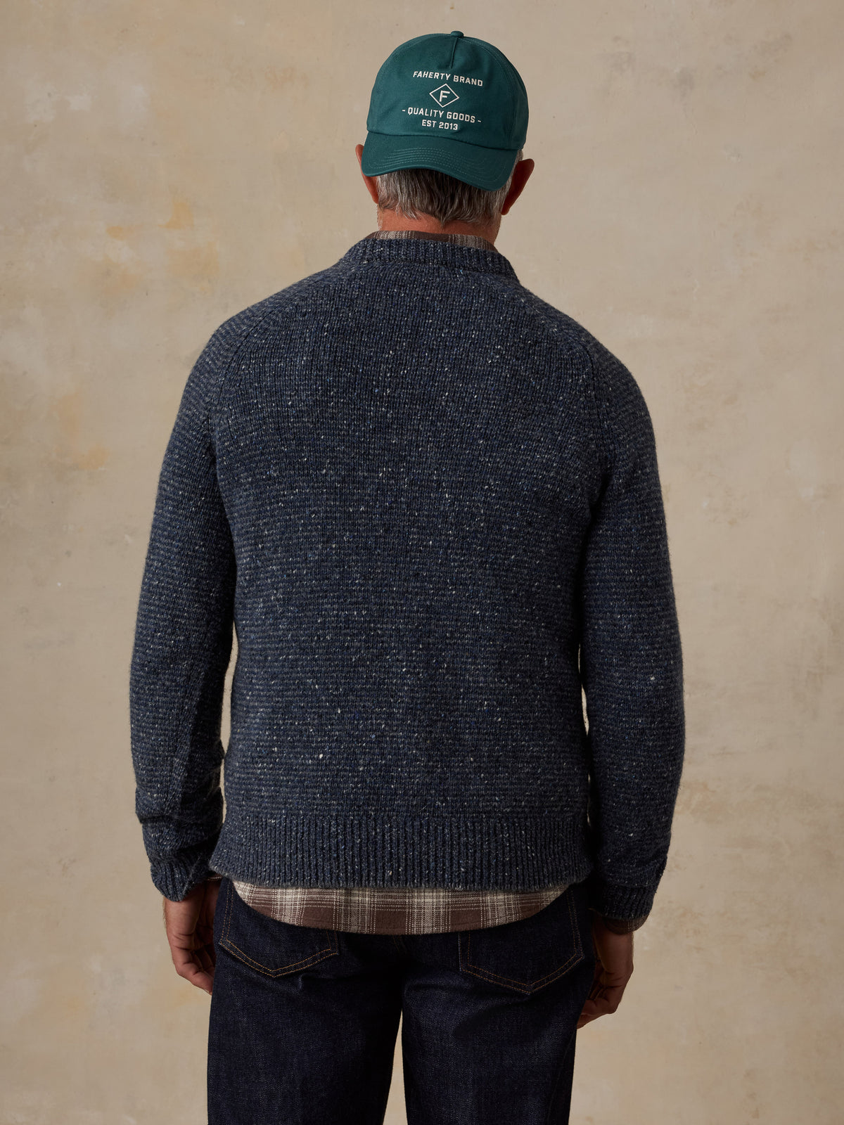 A man viewed from behind wearing a blue sweater and jeans, image 3 of 5
