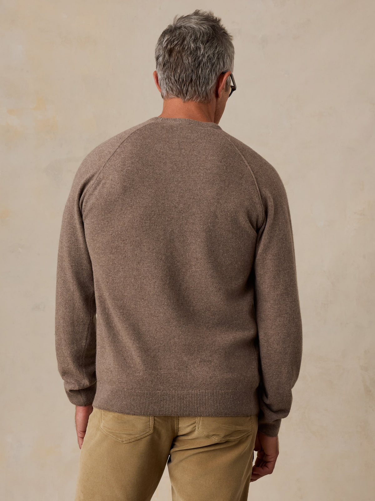 A man viewed from behind wearing a brown sweater and corduroy pants, image 5 of 5