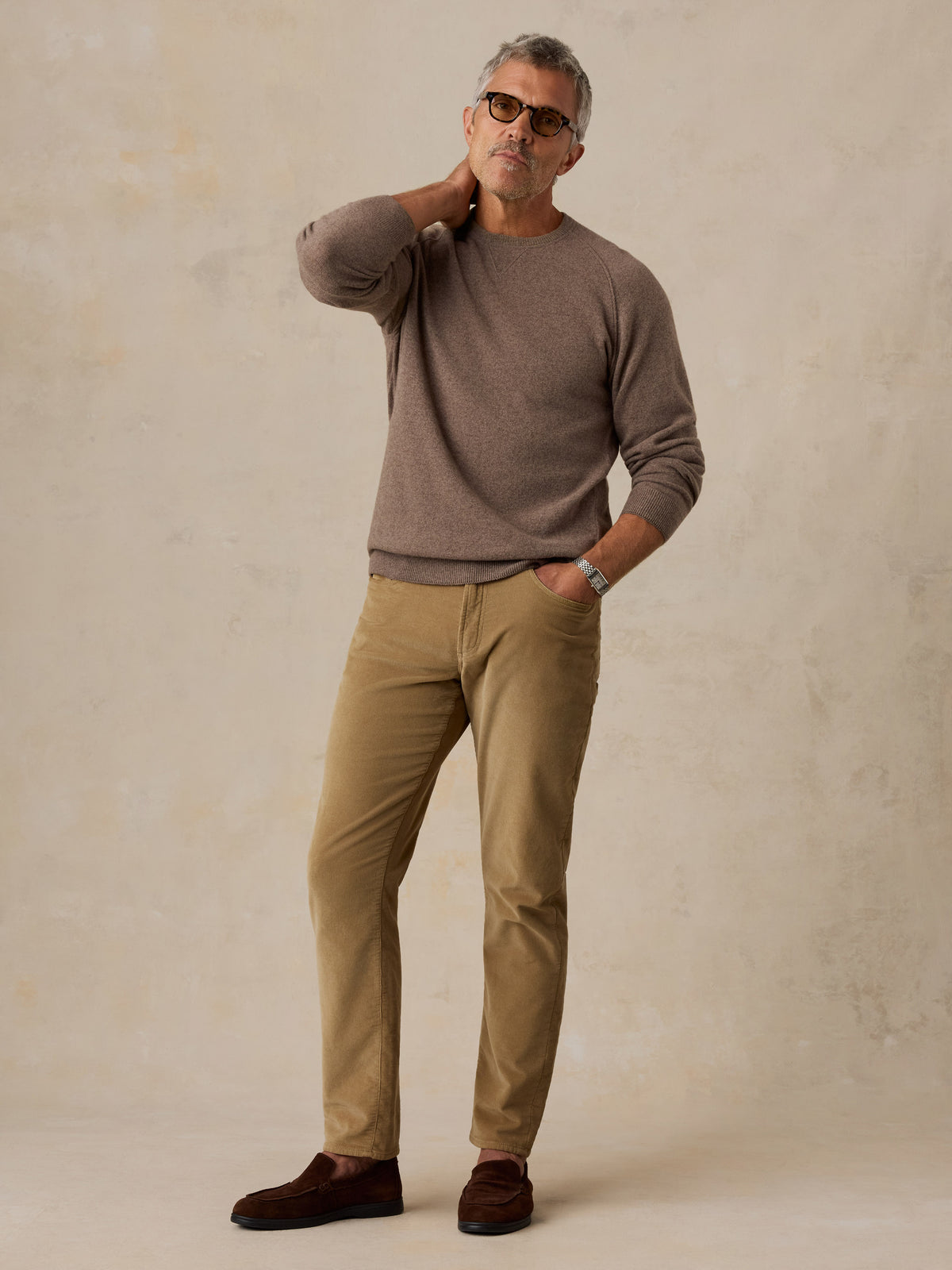 A man wearing a brown sweater and corduroy pants, image 2 of 5