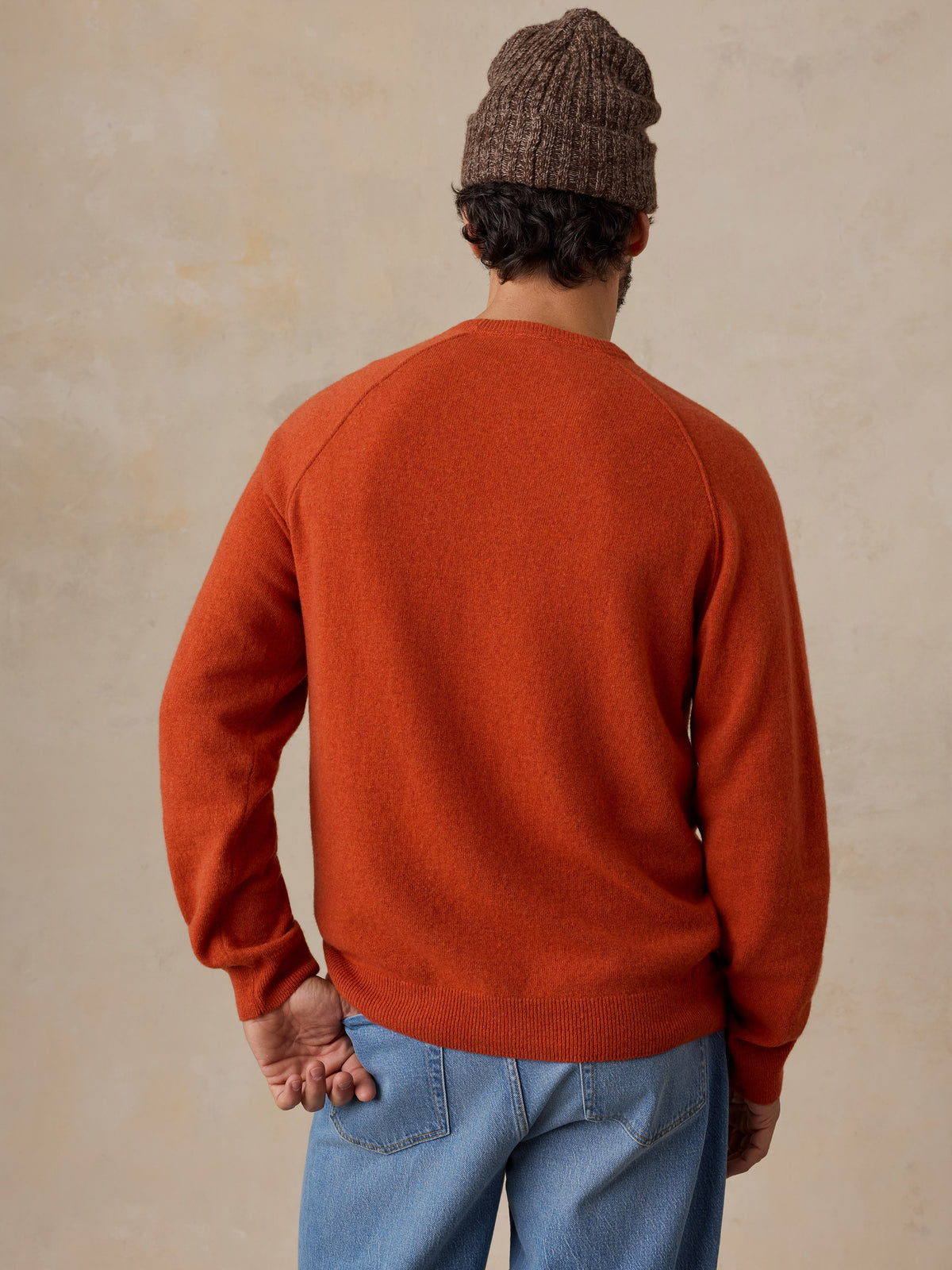 A man viewed from behind wearing an orange sweater and jeans, image 5 of 6
