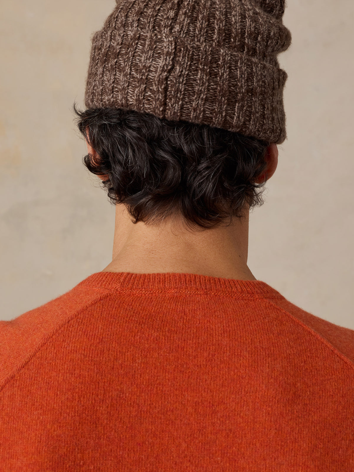 Close up of a man viewed from behind wearing an orange sweater and a beanie, image 6 of 6