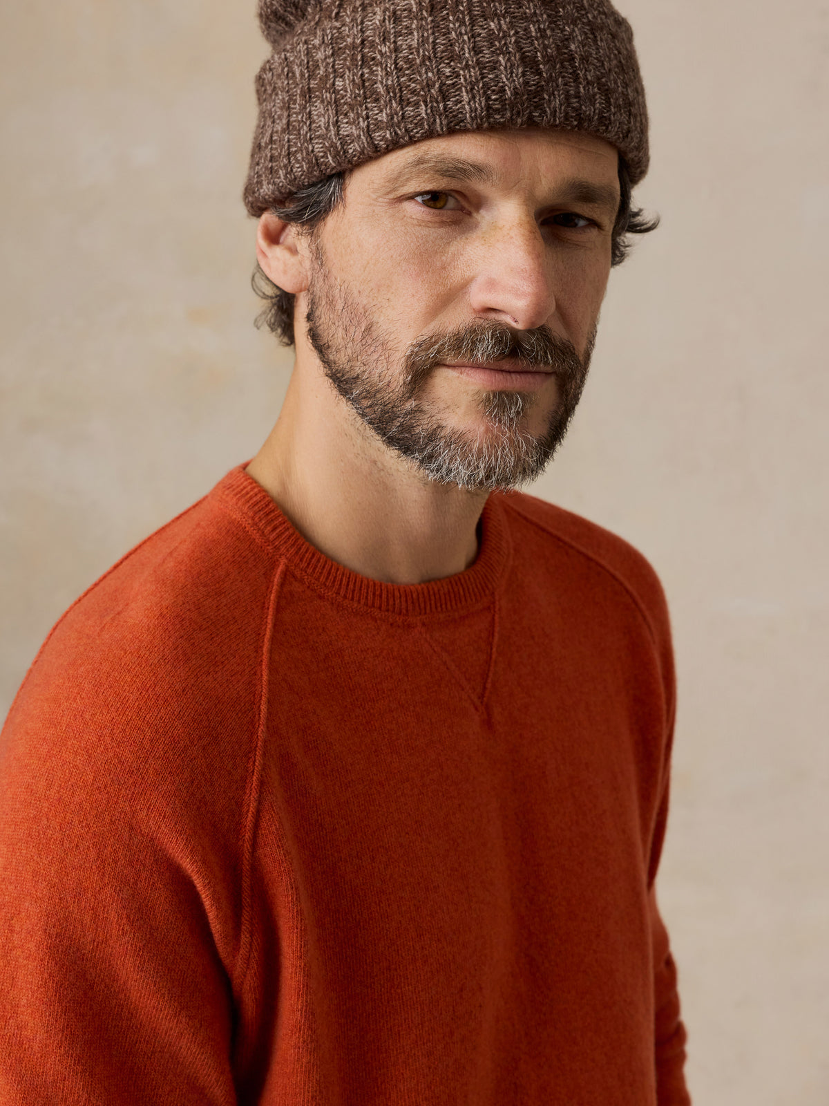 Close up of a man wearing an orange sweater and a beanie, image 4 of 6