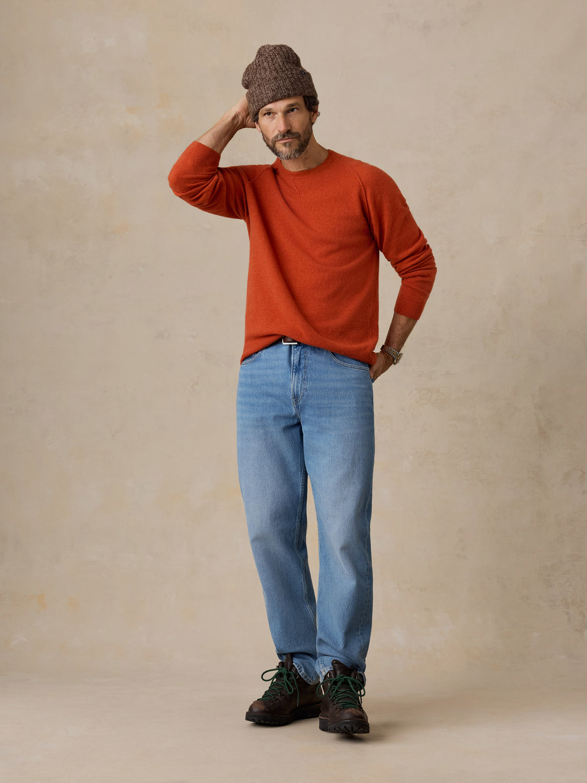 A man wearing an orange sweater and a jeans, image 2 of 6