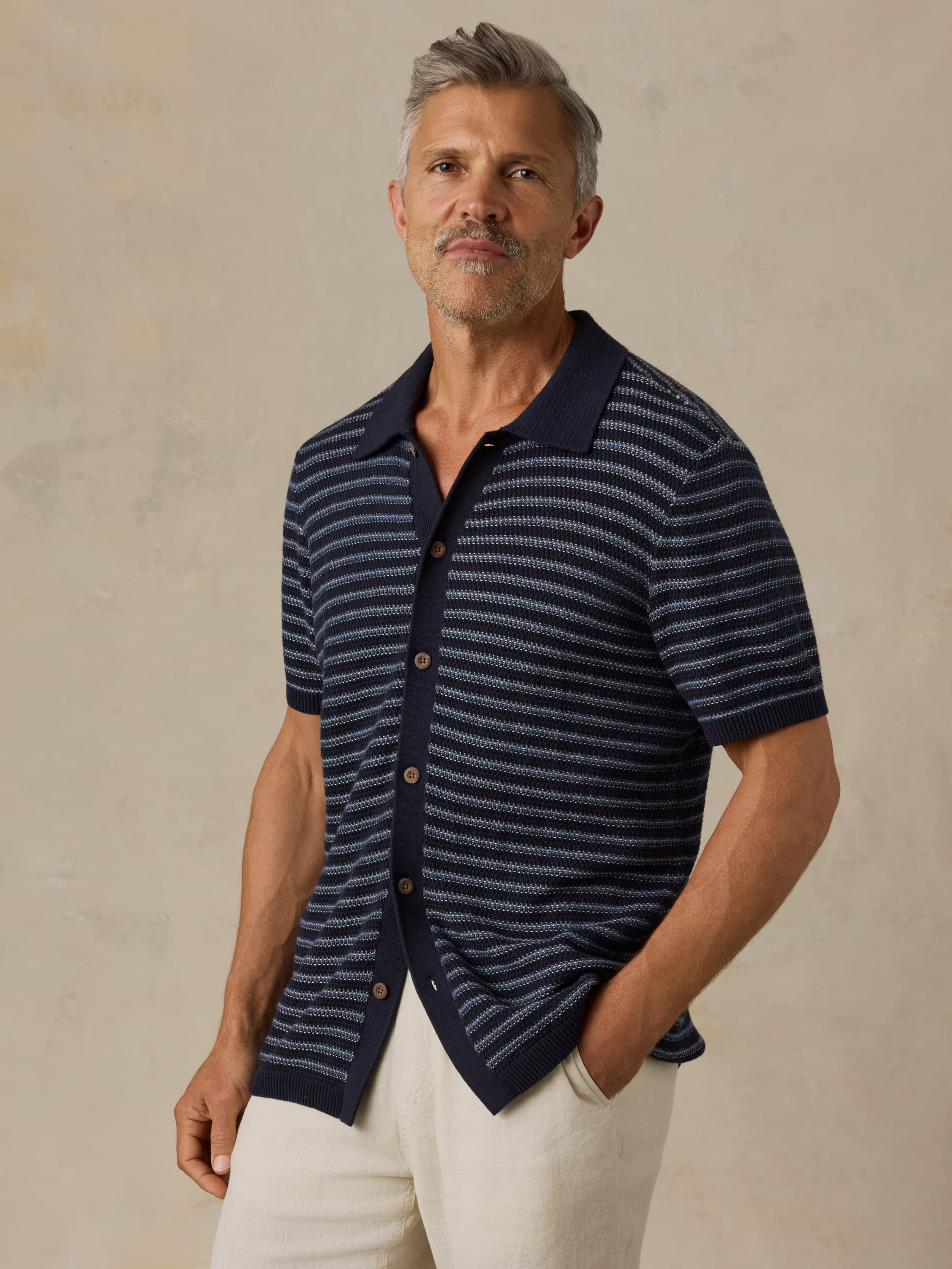 Man wearing a navy striped short-sleeve shirt with a light colored pants against a beige background