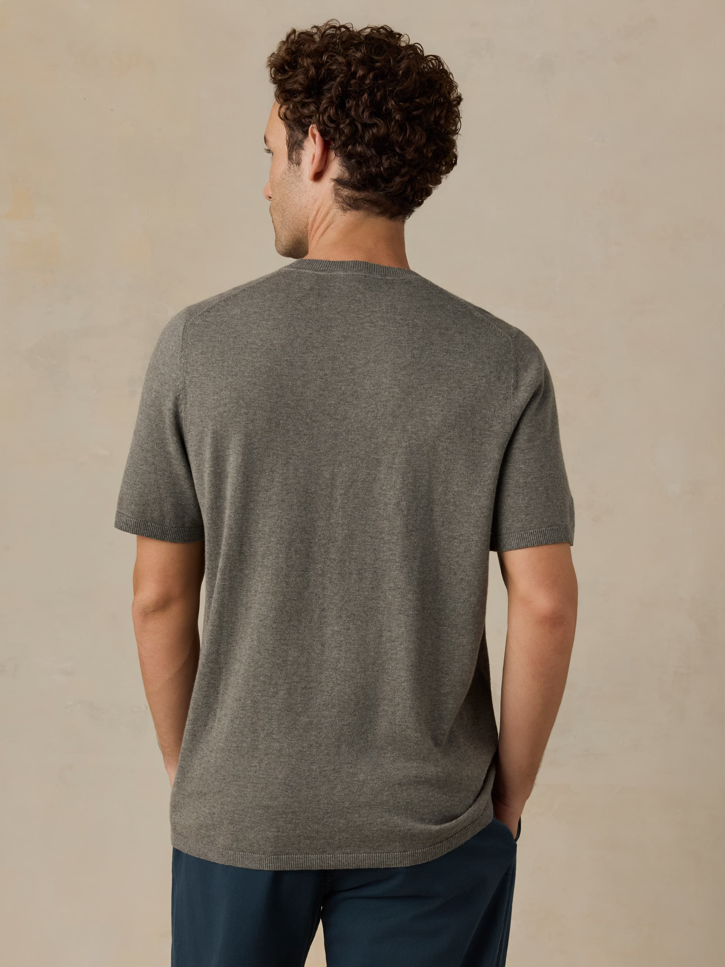 Man wearing a green t-shirt and dark blue pants against a beige background