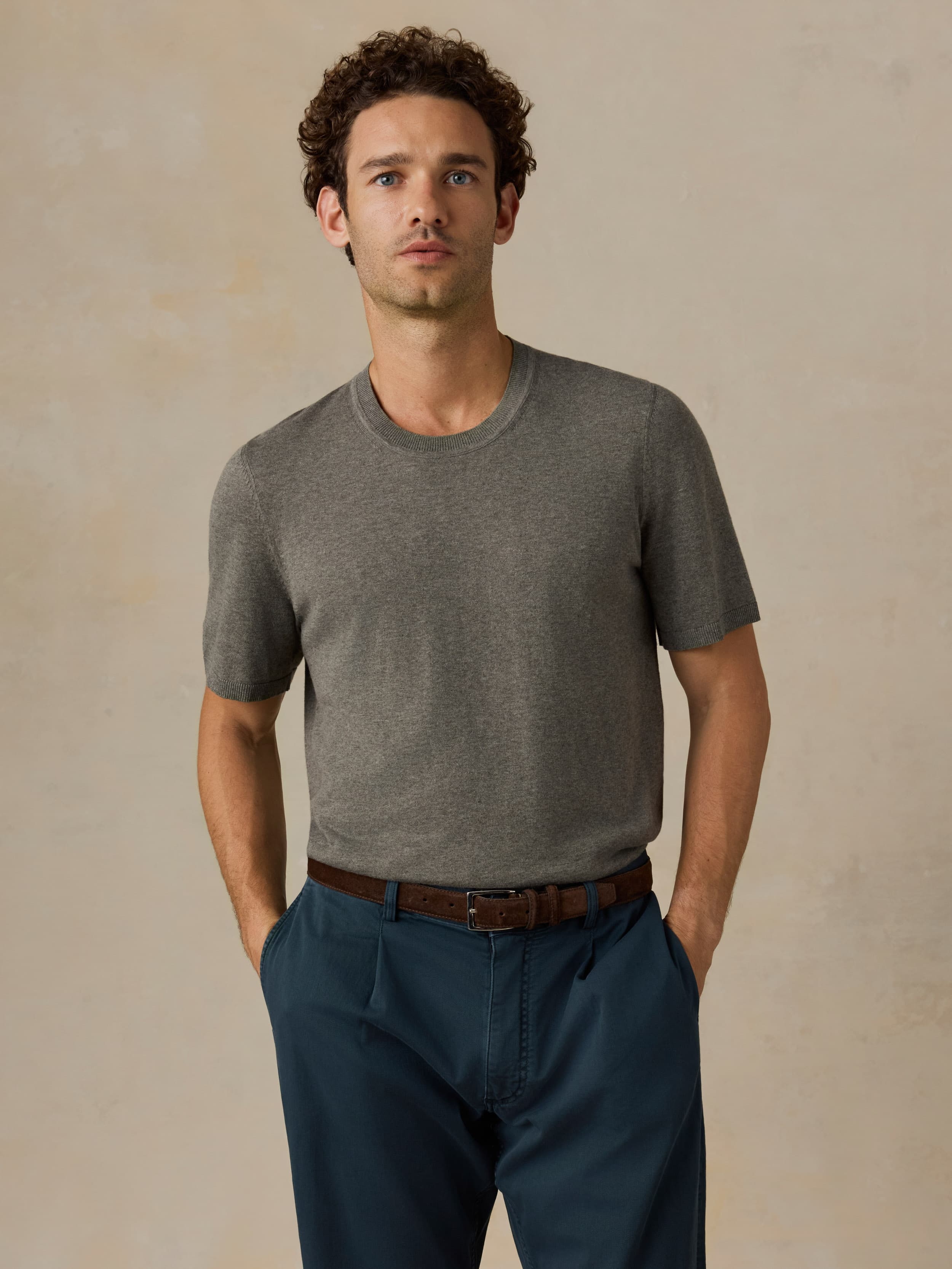 Man wearing a green t-shirt and dark blue pants against a beige background