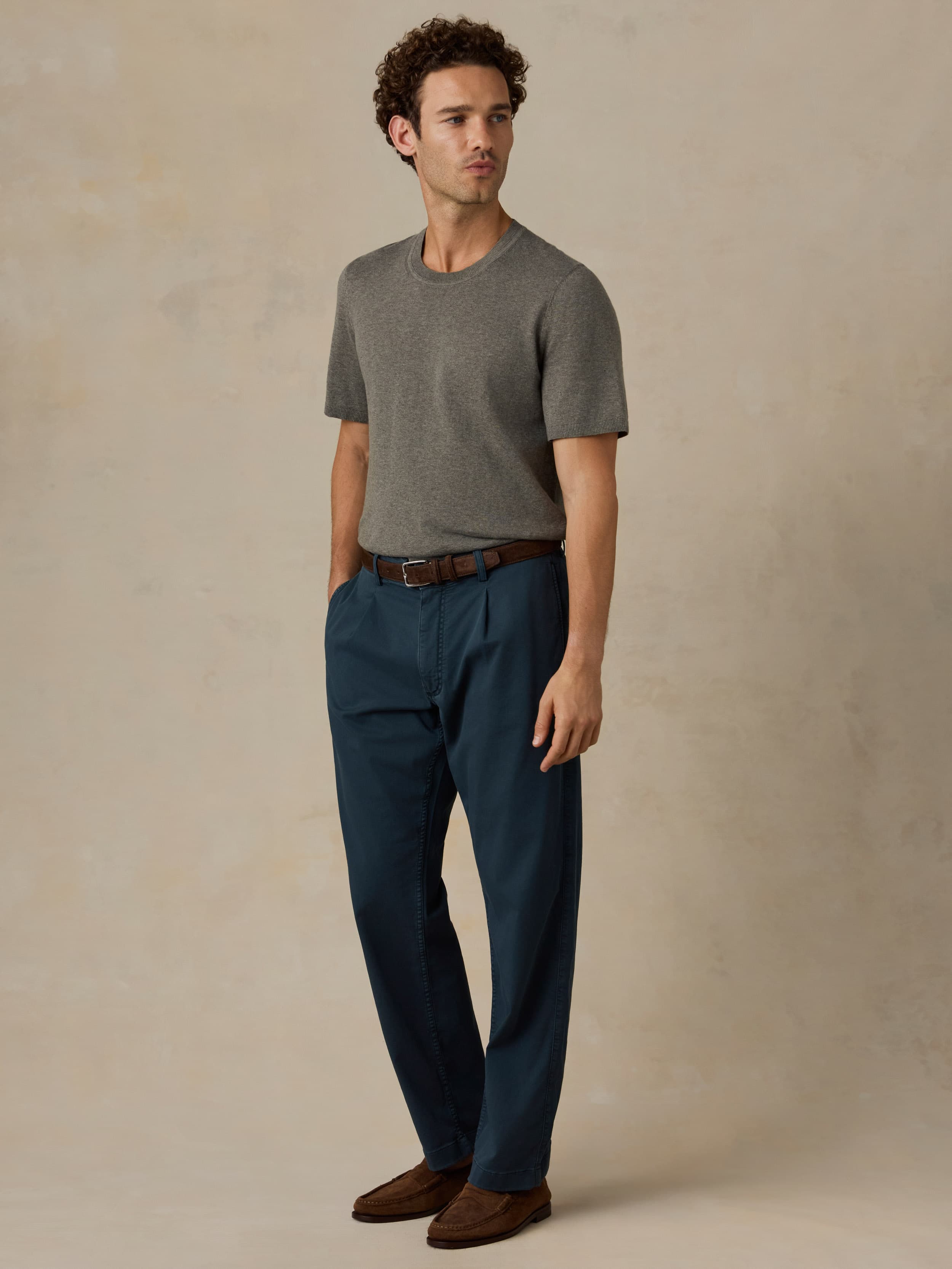 Man wearing a green t-shirt and dark blue pants against a beige background