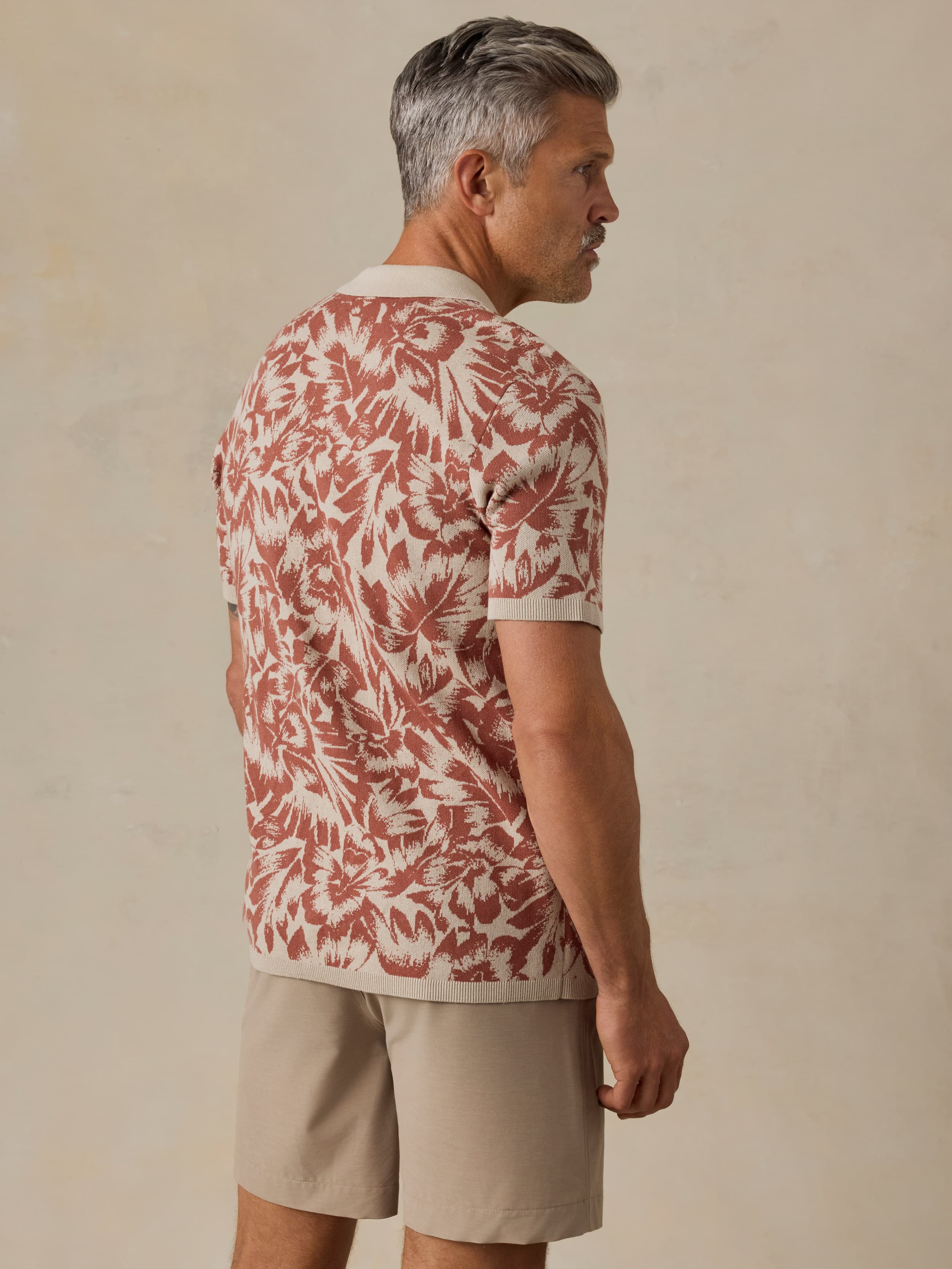 Man wearing a red and white floral patterned shirt with beige shorts against a beige background