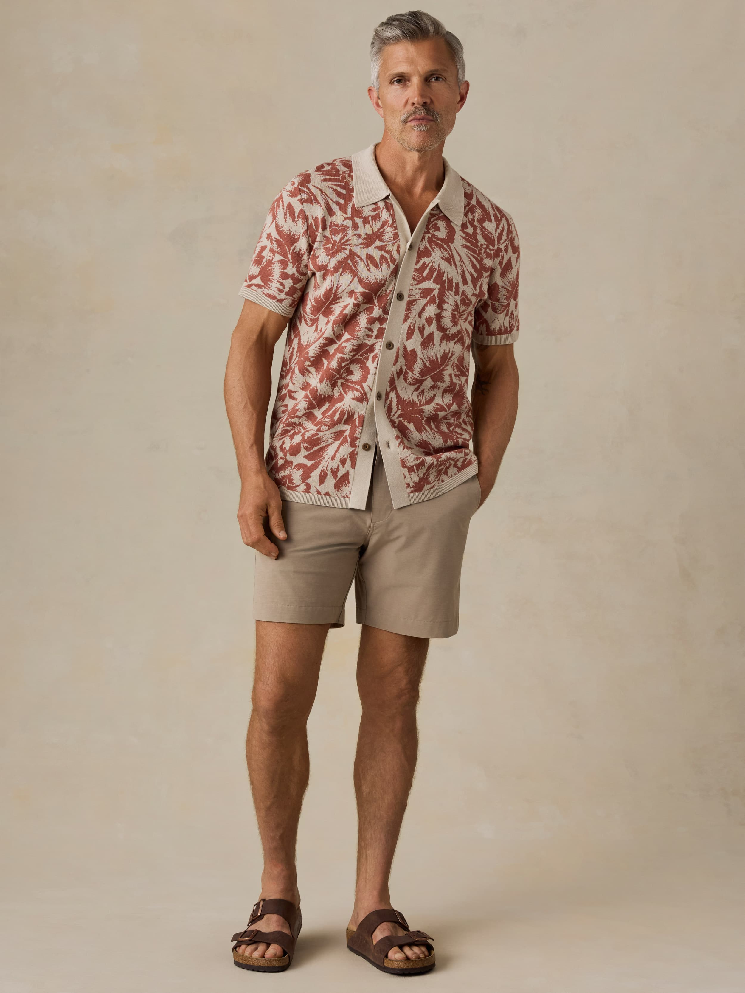 Man wearing a red and white floral patterned shirt with beige shorts against a beige background
