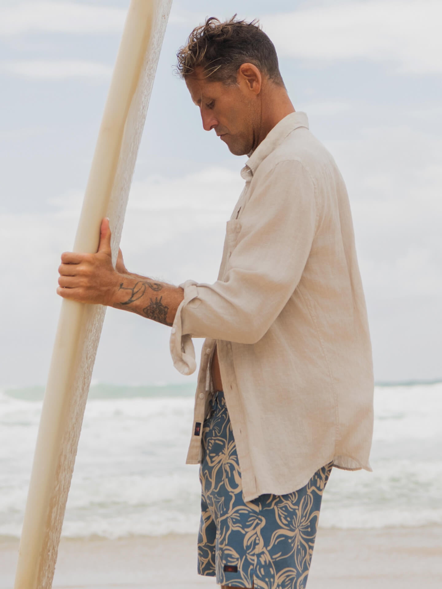 a male surfer wearing a laguna linen shirt over board shorts holding a surf board