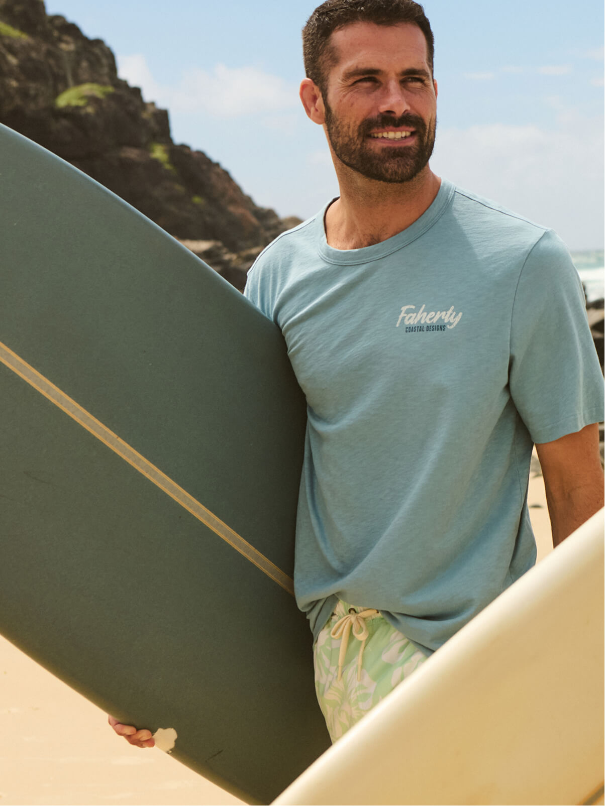 man holding surf board wearing Faherty graphic tee