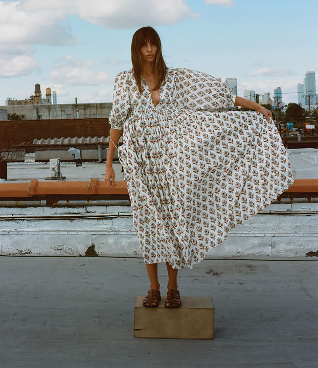 famale model wearing floral print dress standing on an apple box, on a rooftop infront of urban landscape