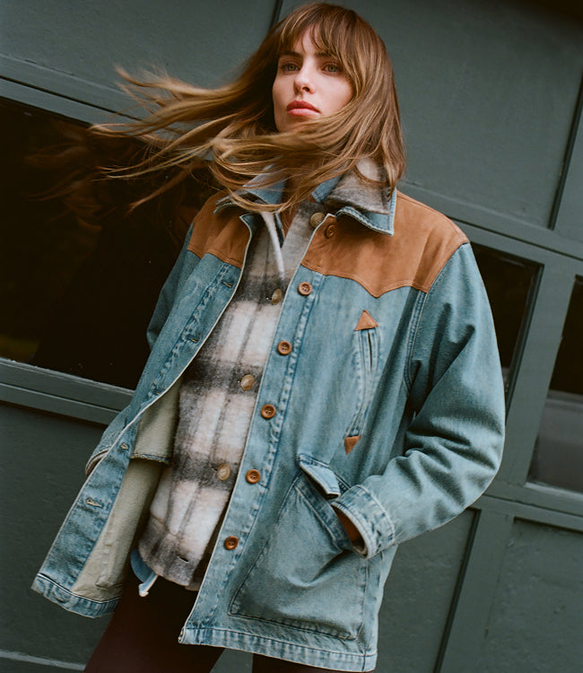 Female model with wind blowing through her hair wearing a wool CPO with a denim range jacket layered over it