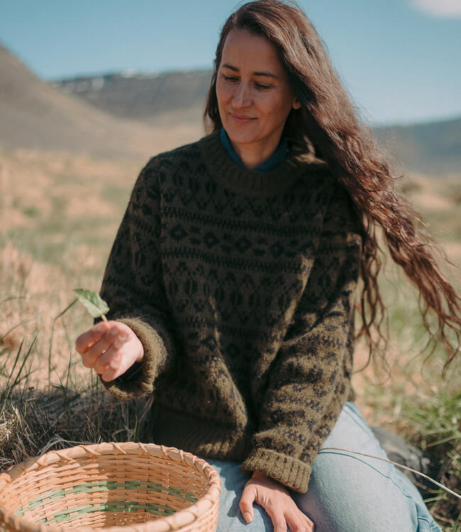 Woman sitting in a field wearing a sweater foraging for plants