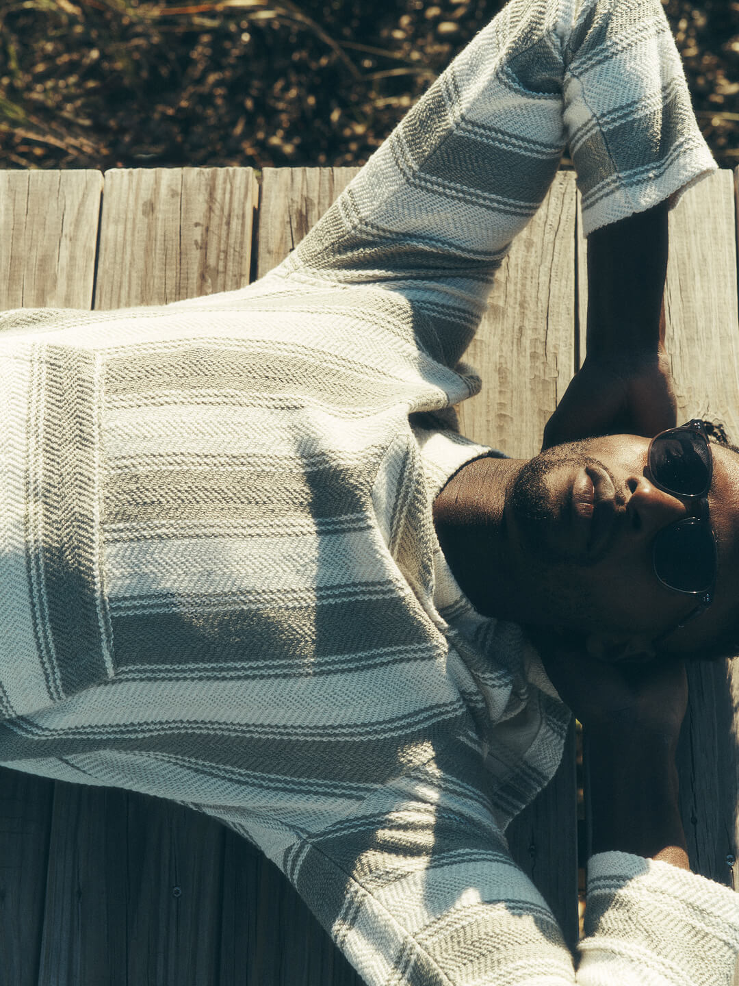 man lying on his back on a dock wearing a knit hoodie and sunglasses