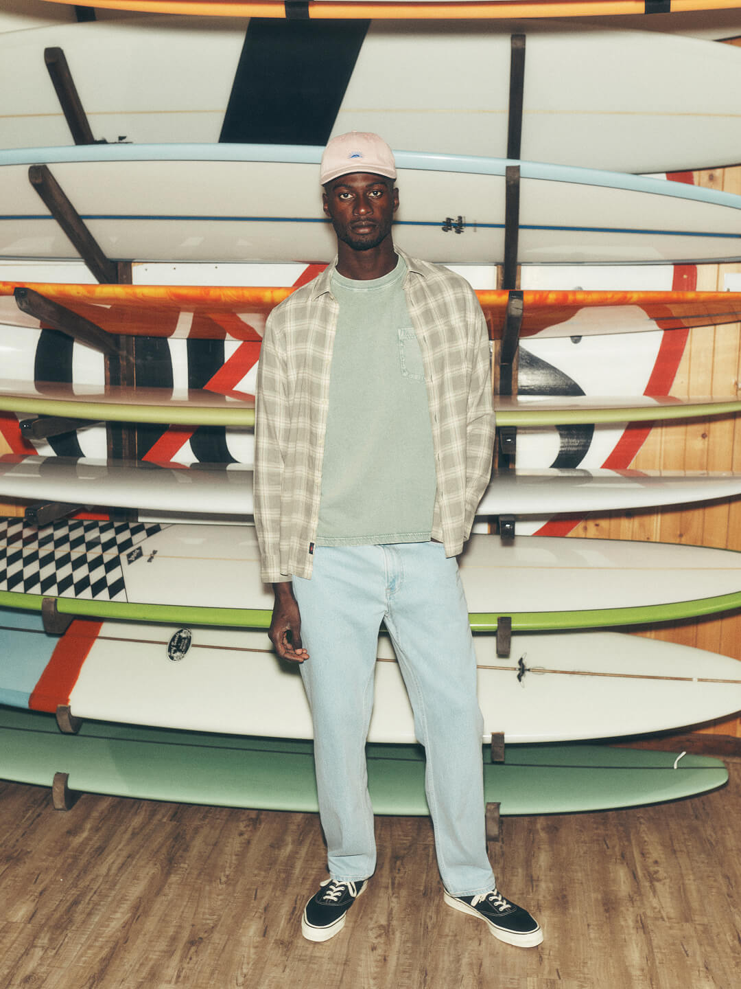 A male model dressed in surf revival collection standing in front of a rach of surf boards