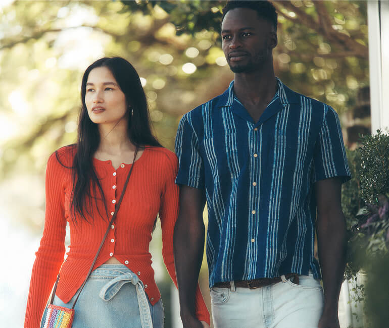A couple walking down the street in Charleston, the woman wearing a pointelle cardigan and a denim dress, the man wearing a blue striped camp shirt