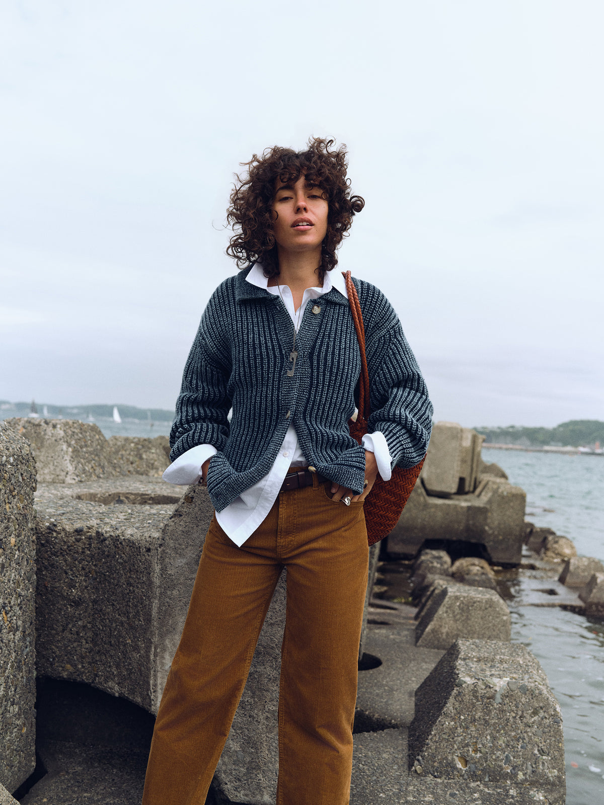 A woman wearing a blue sweater over a white button up shirt and tan corduroy pants, image 1 of 8