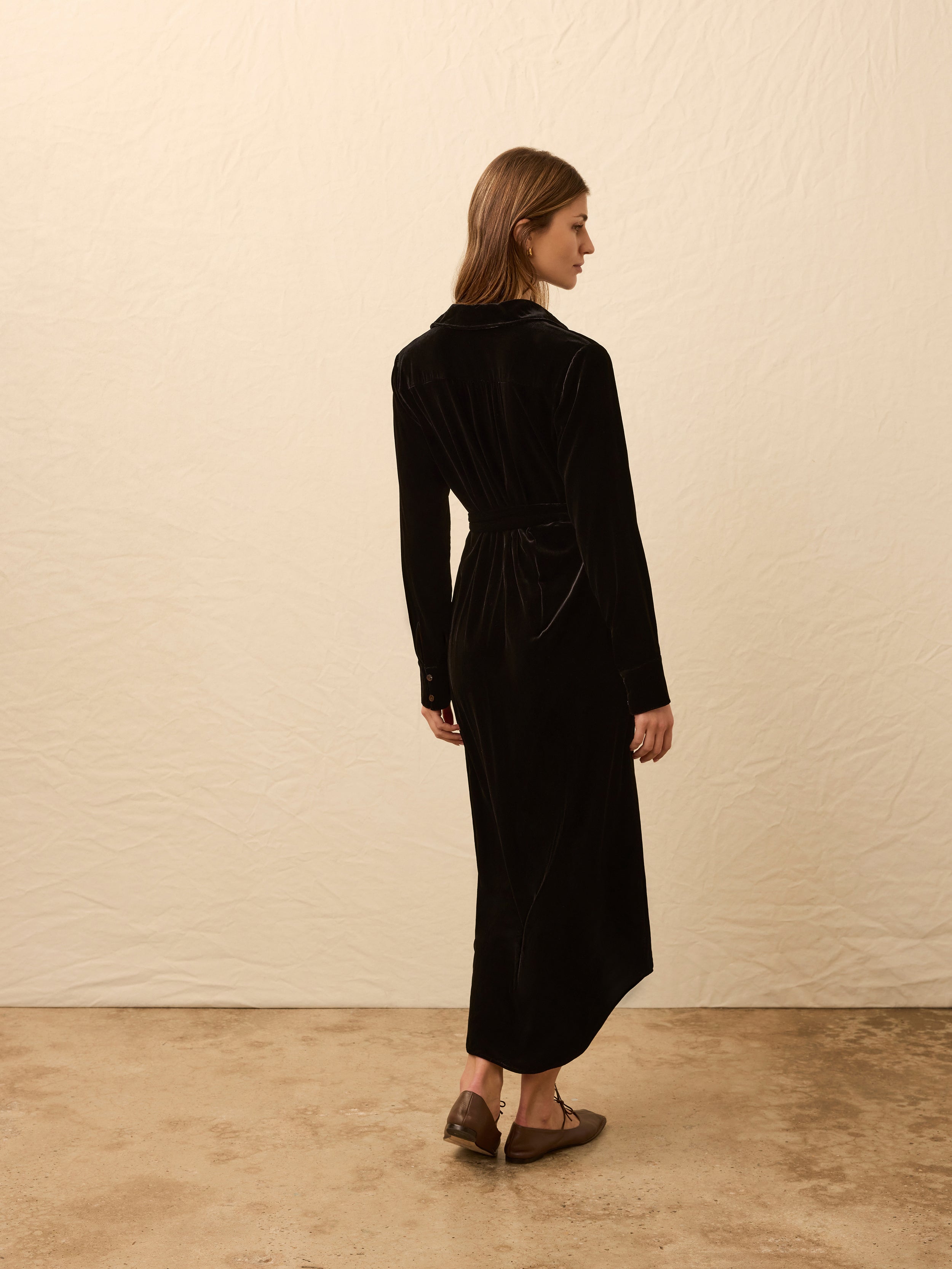 Woman wearing a black velvet long sleeve wrap dress against a beige background