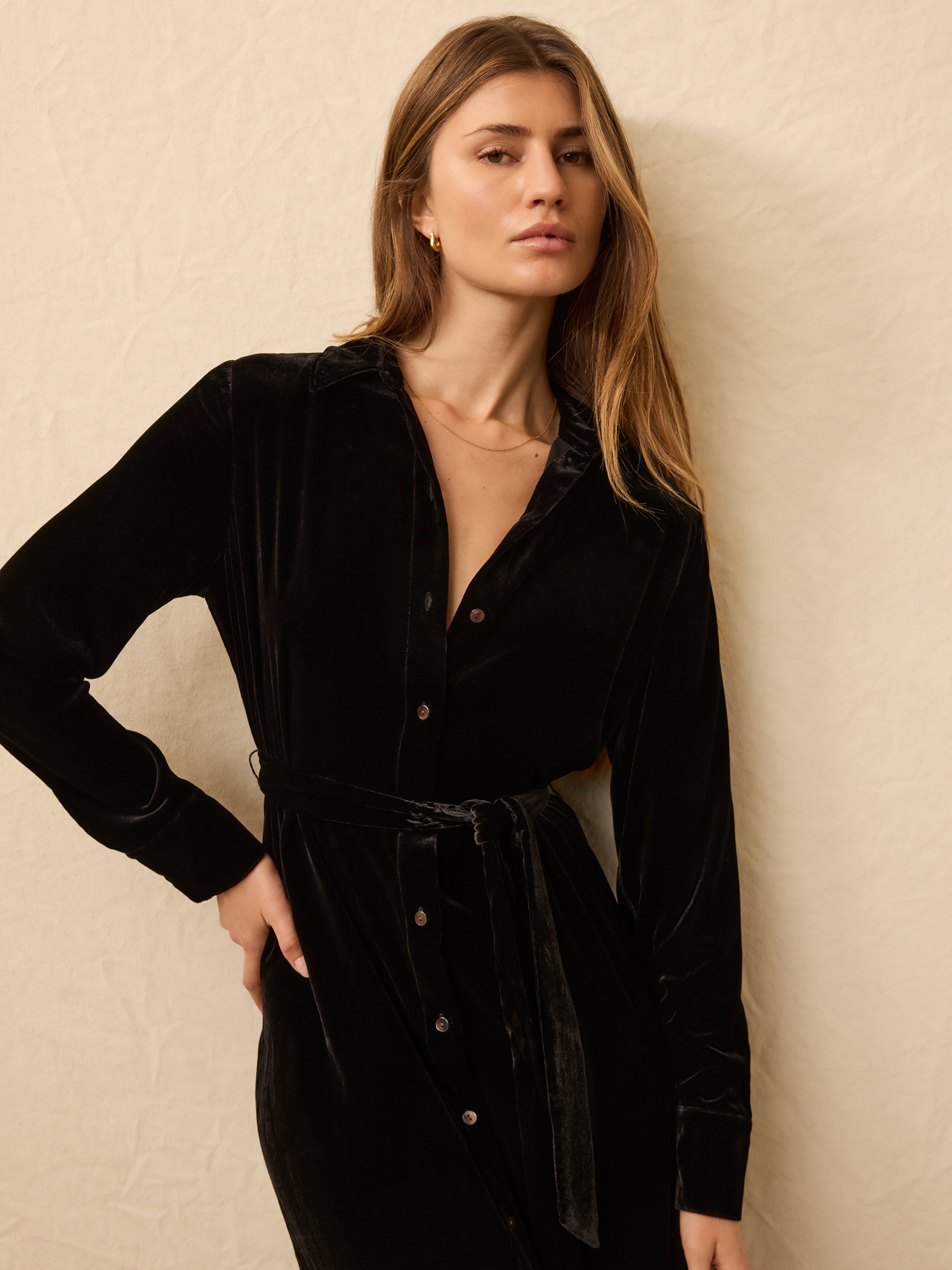 Woman wearing a black velvet long sleeve wrap dress against a beige background