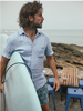 Alex Faherty on the beach with a surfboard, wearing Palma Linen shirt and boardshorts.
