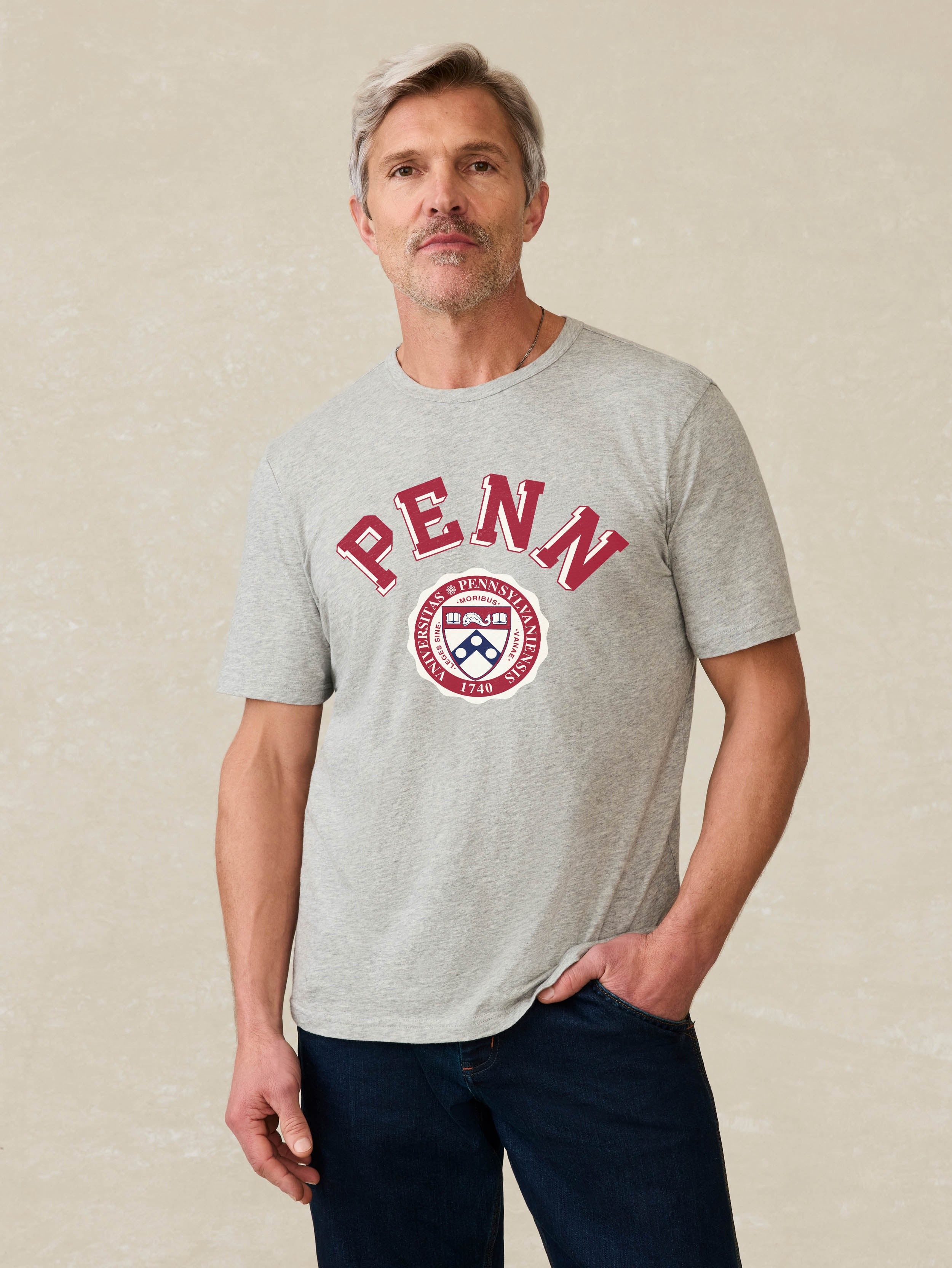 Man wearing a grey t-shirt with University of Pennsylvania graphic at the front against a beige background