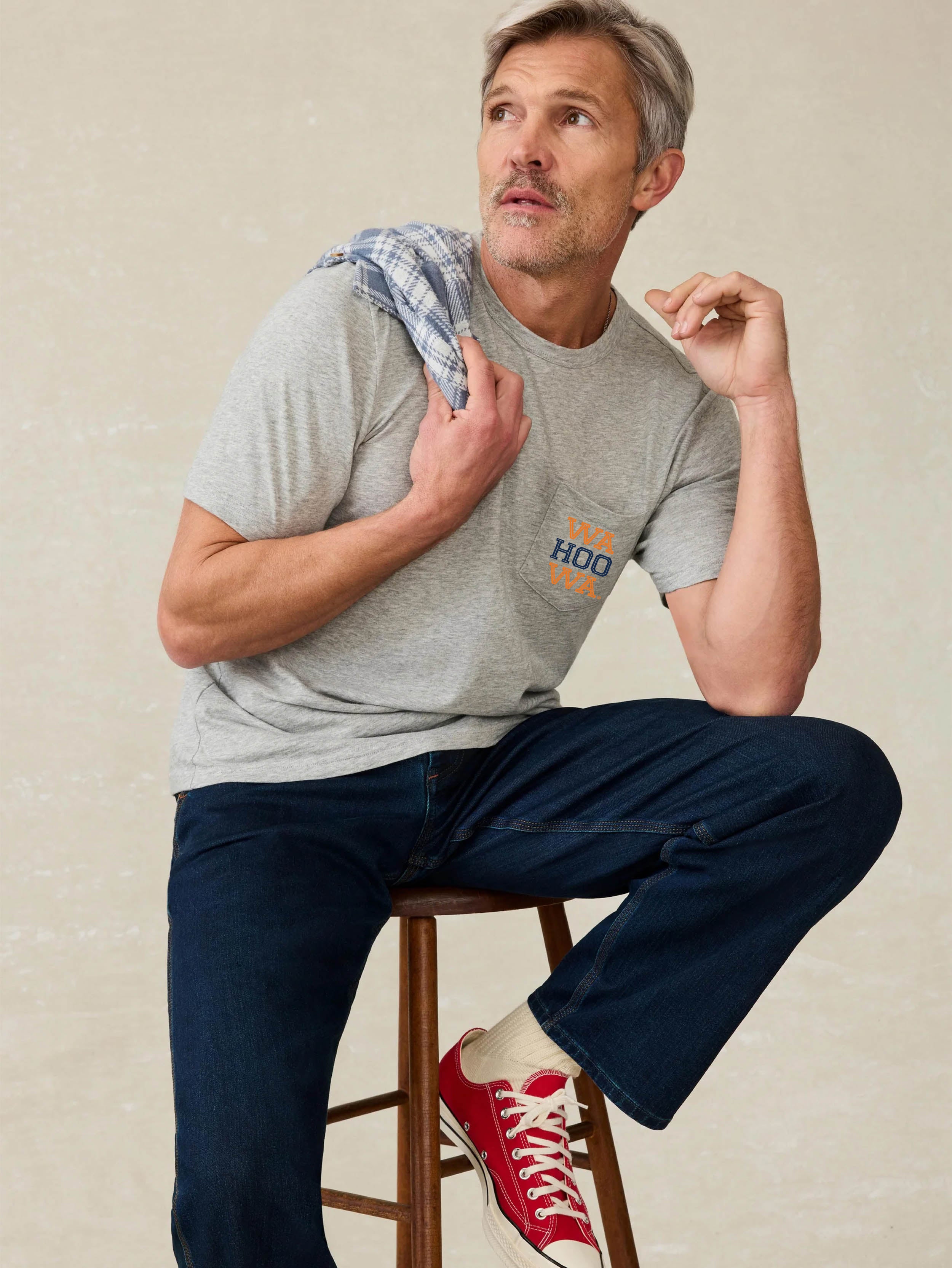 Man wearing a grey short sleeve t-shirt with University of Virginia graphic on front chest pocket against a beige background
