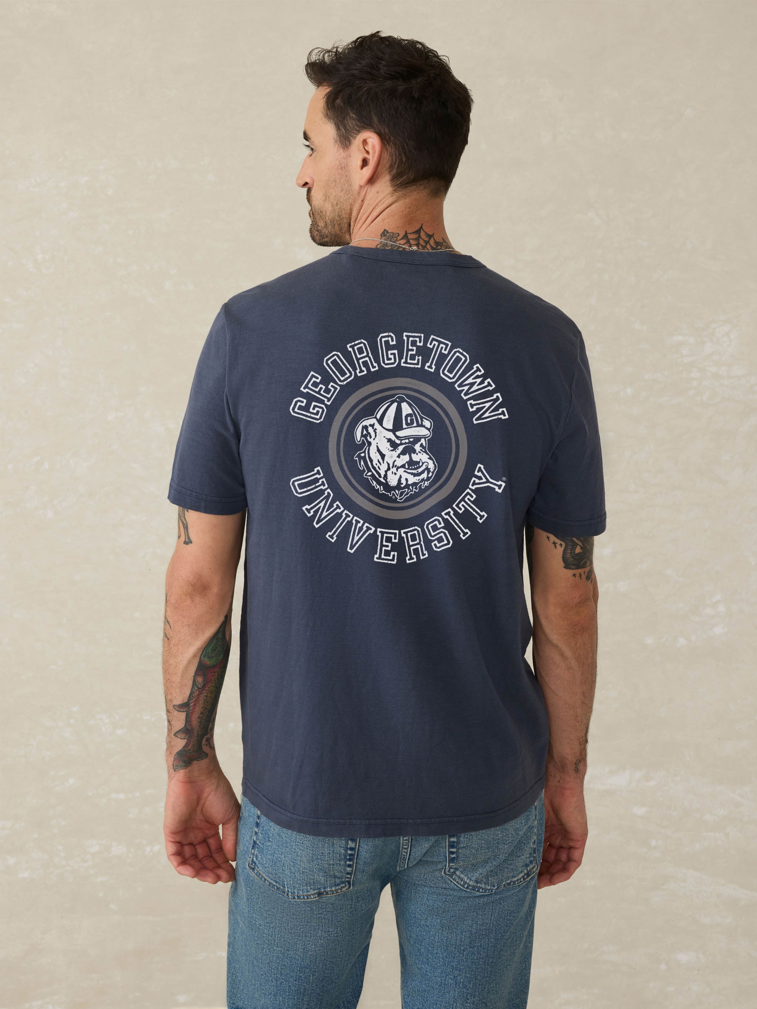 Man wearing a navy blue short sleeve t-shirt with Georgetown graphic on the center back against a beige background