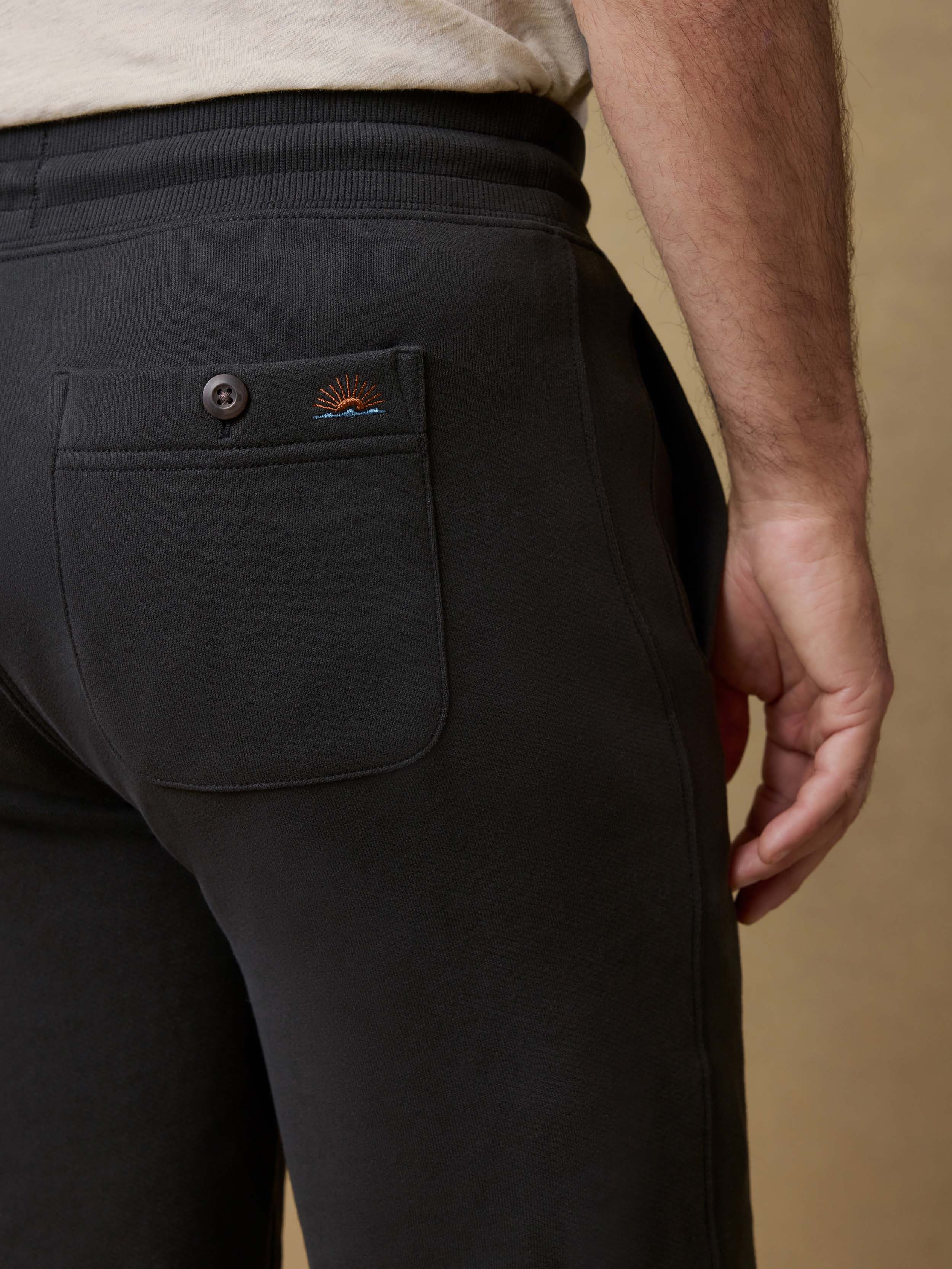 Detail back view of a man wearing black jogger sweatpants with a white t-shirt on a beige background