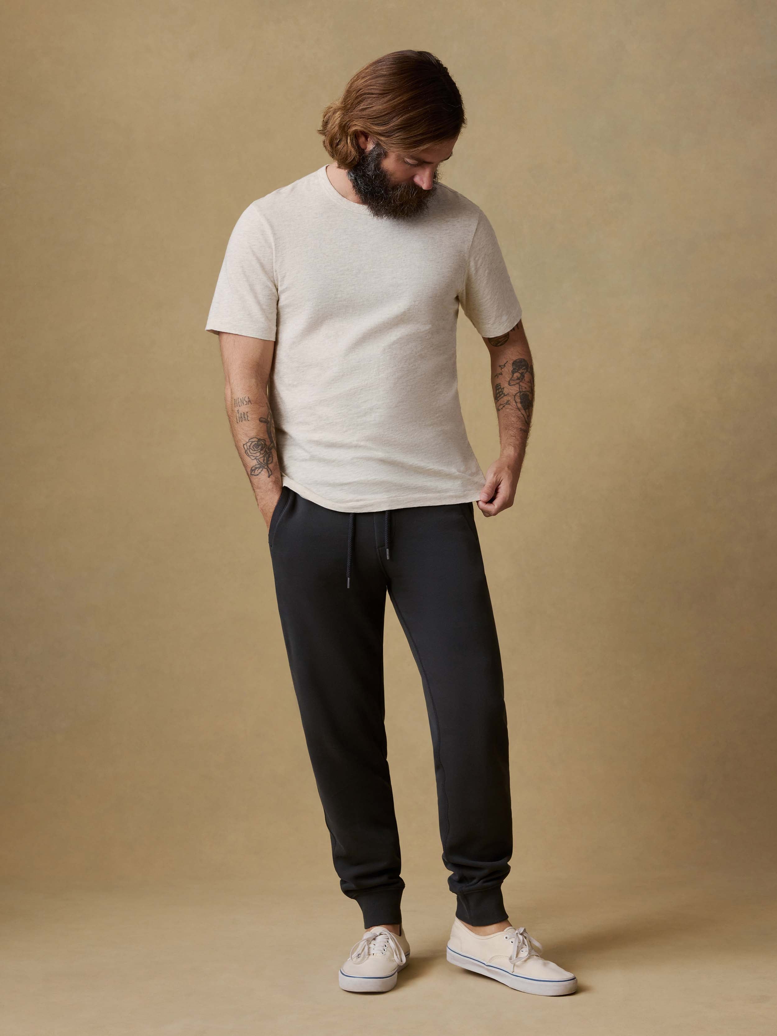 Man wearing black jogger sweatpants with a white t-shirt and white sneakers on a beige background