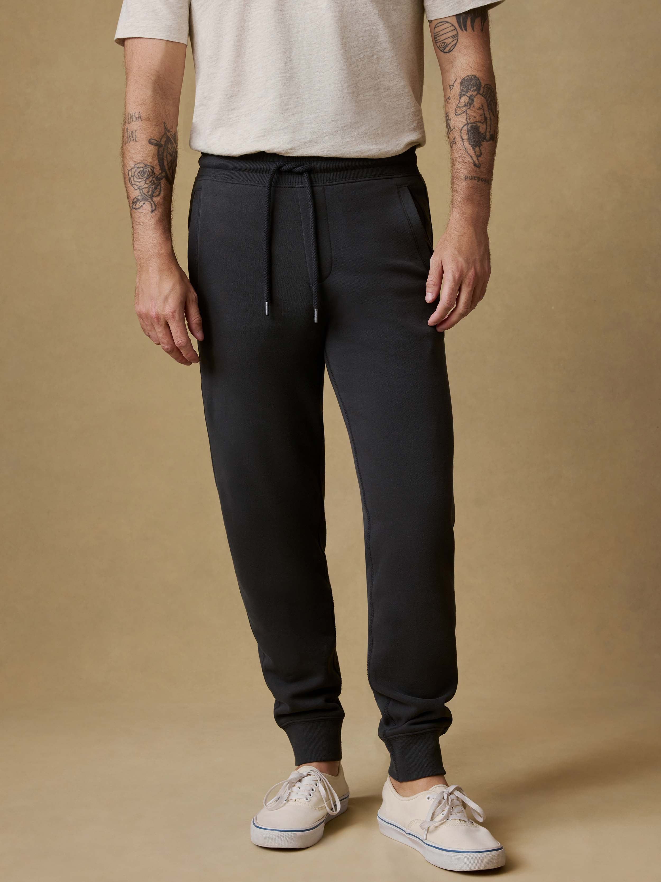 Man wearing black jogger sweatpants with a white t-shirt and white sneakers on a beige background