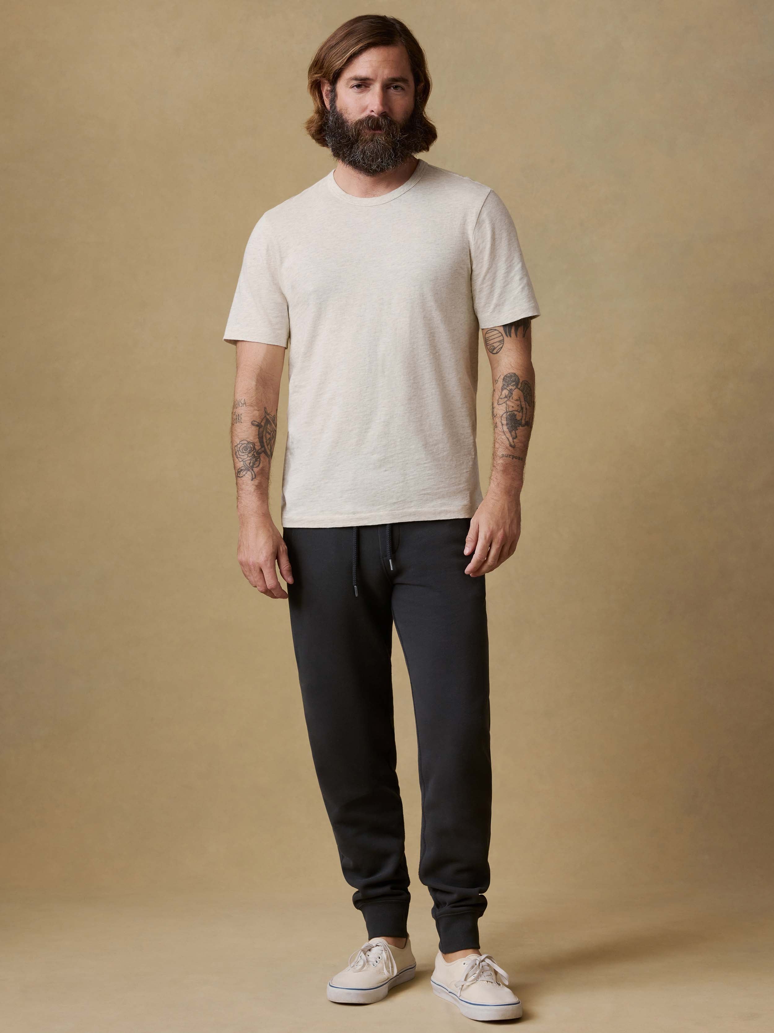 Man wearing black jogger sweatpants with a white t-shirt and white sneakers on a beige background