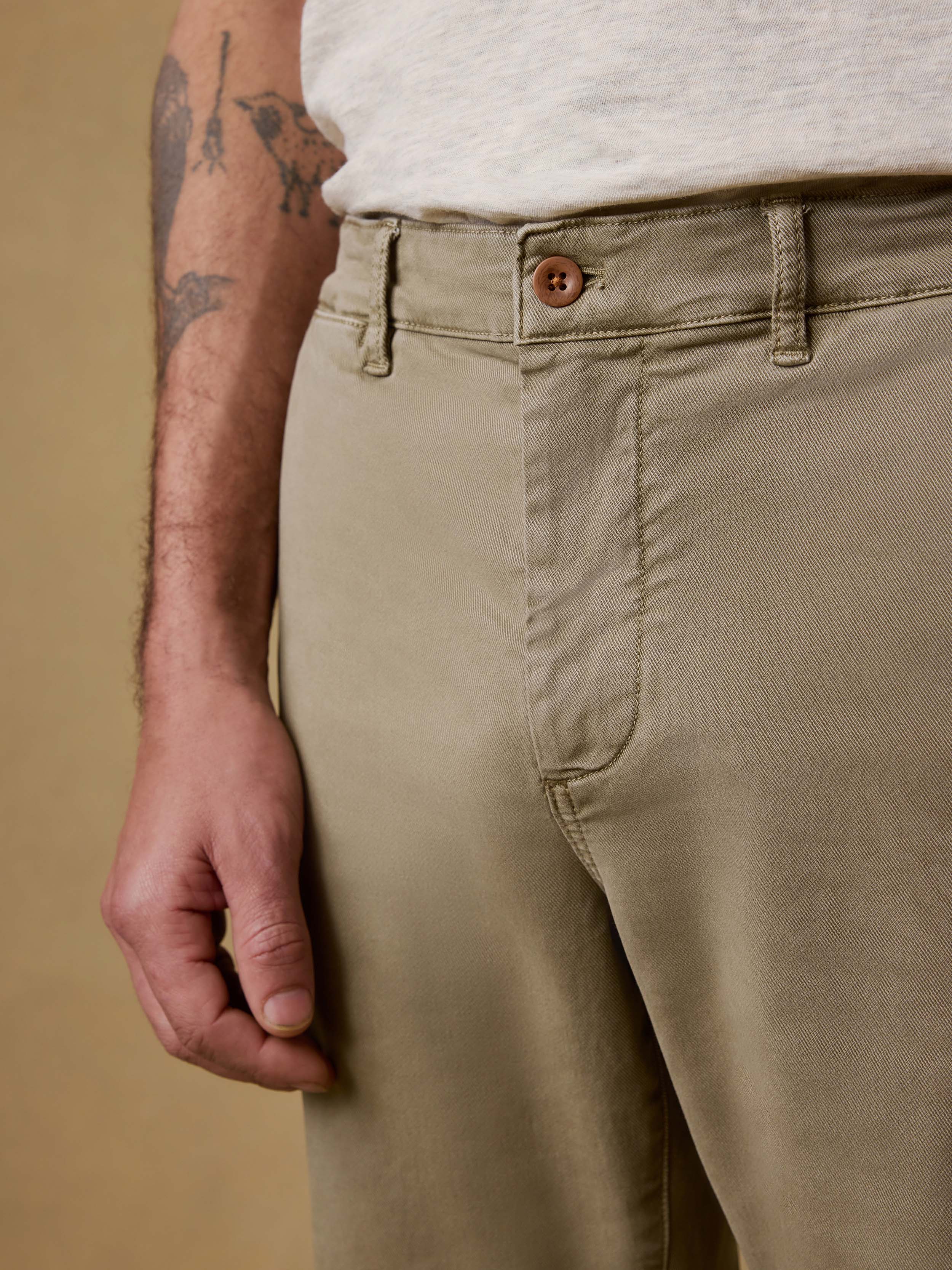 Detail front view of man wearing olive pants with a white t-shirt against a beige background