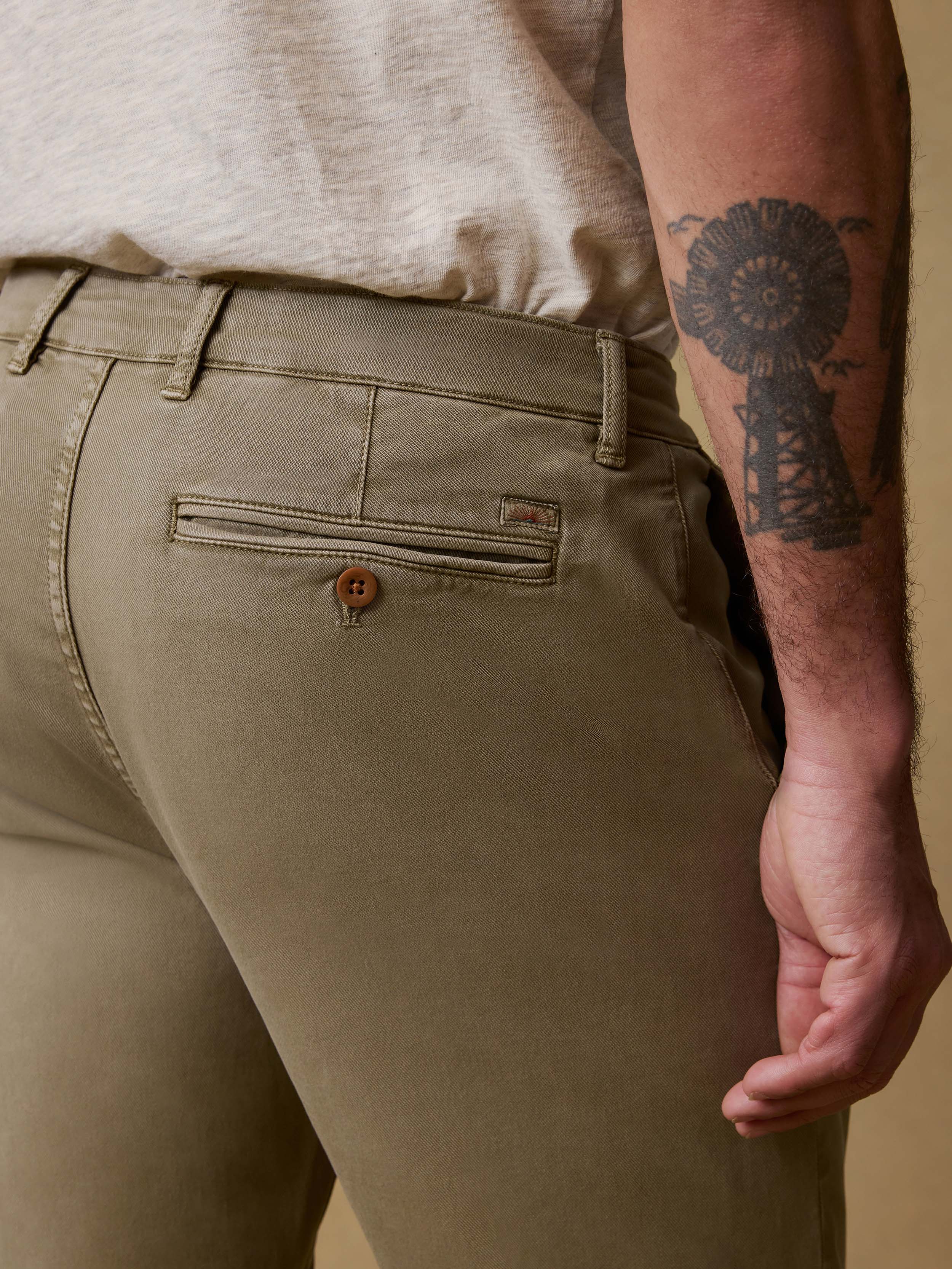 Detail back view of man wearing olive pants and a white t-shirt against a beige background