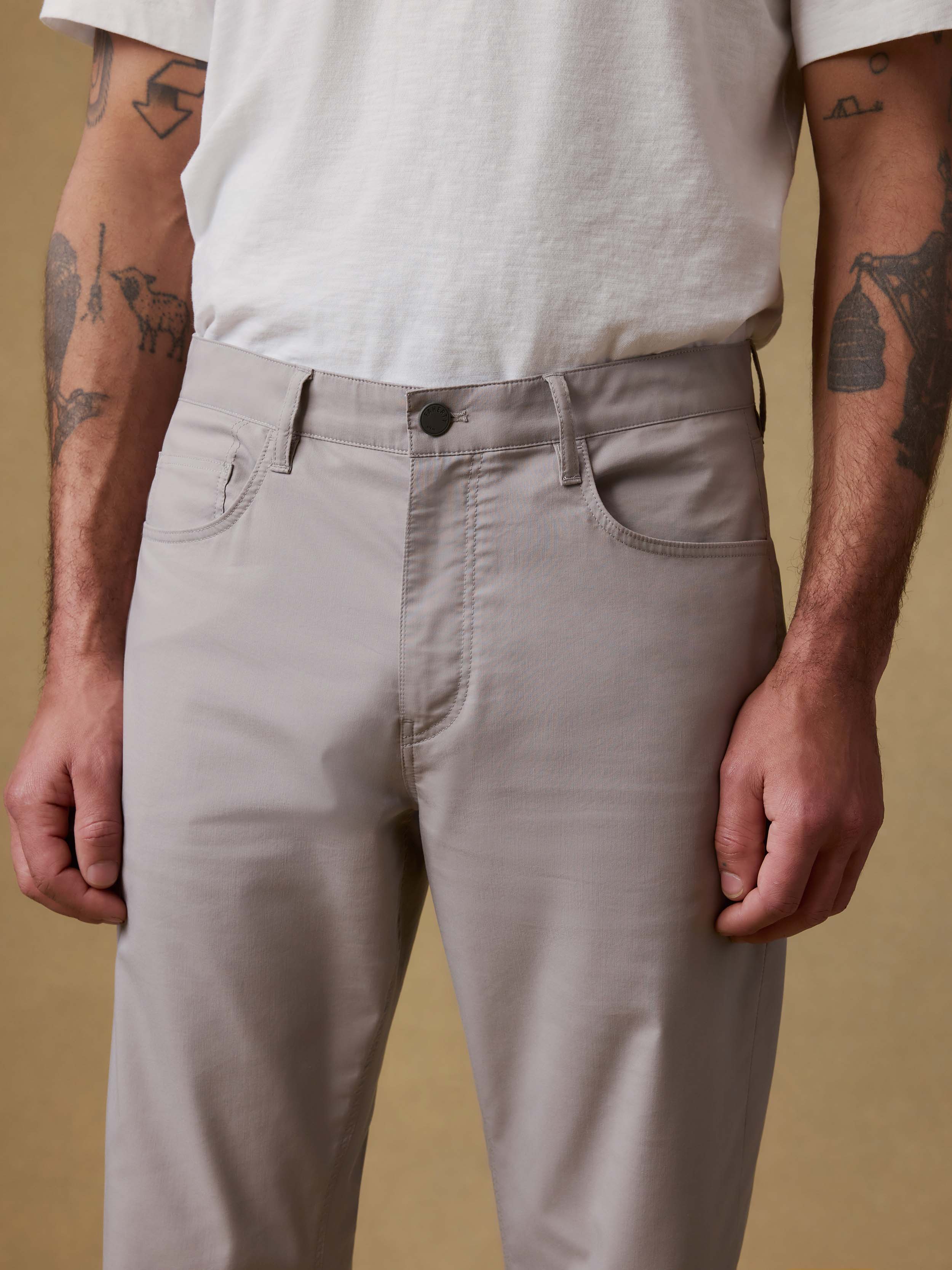 Detail front view of a man wearing light gray pants with a white t-shirt against a beige background