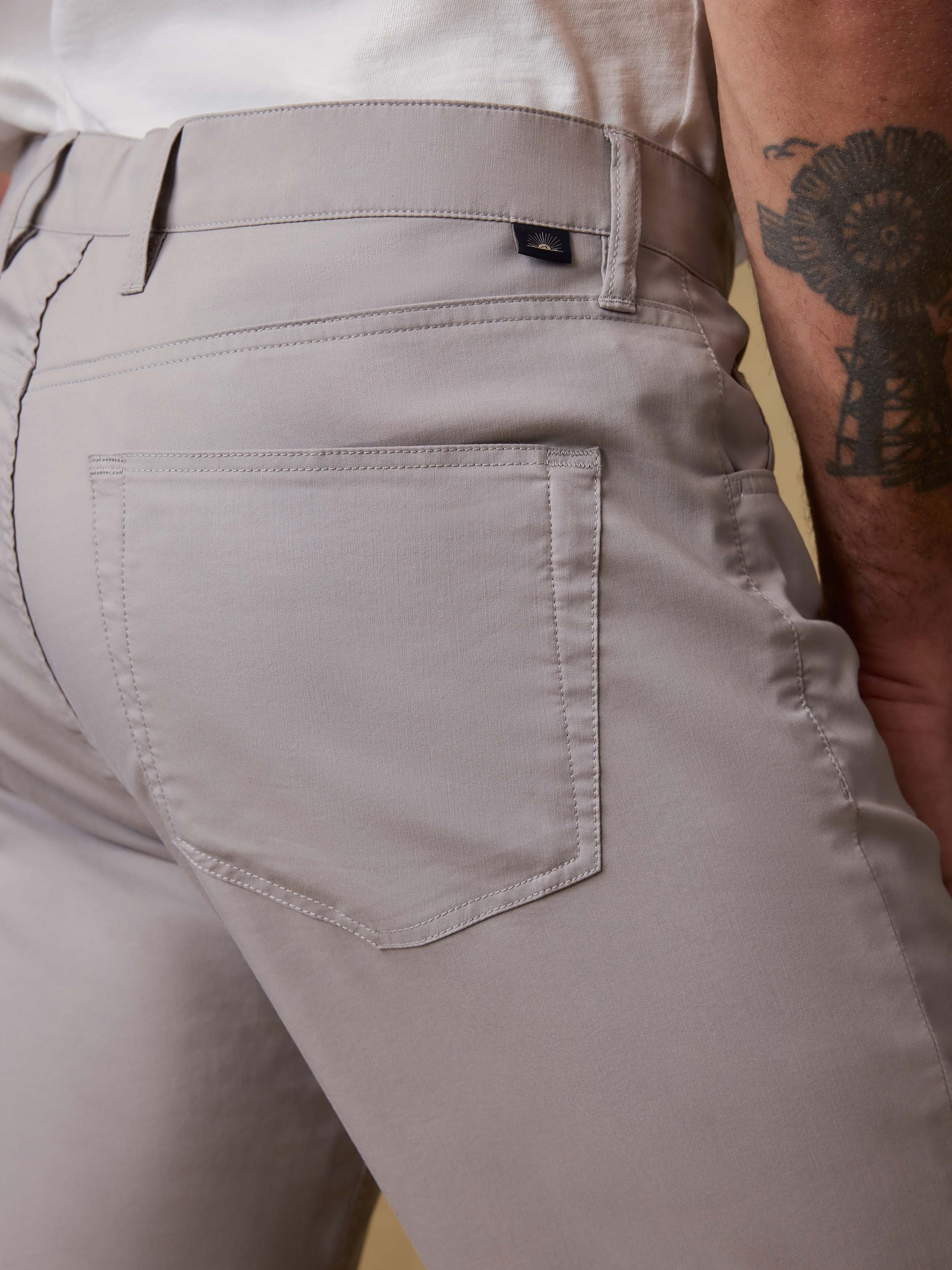 Detail back view of a man wearing light gray pants and a white t-shirt against a beige background