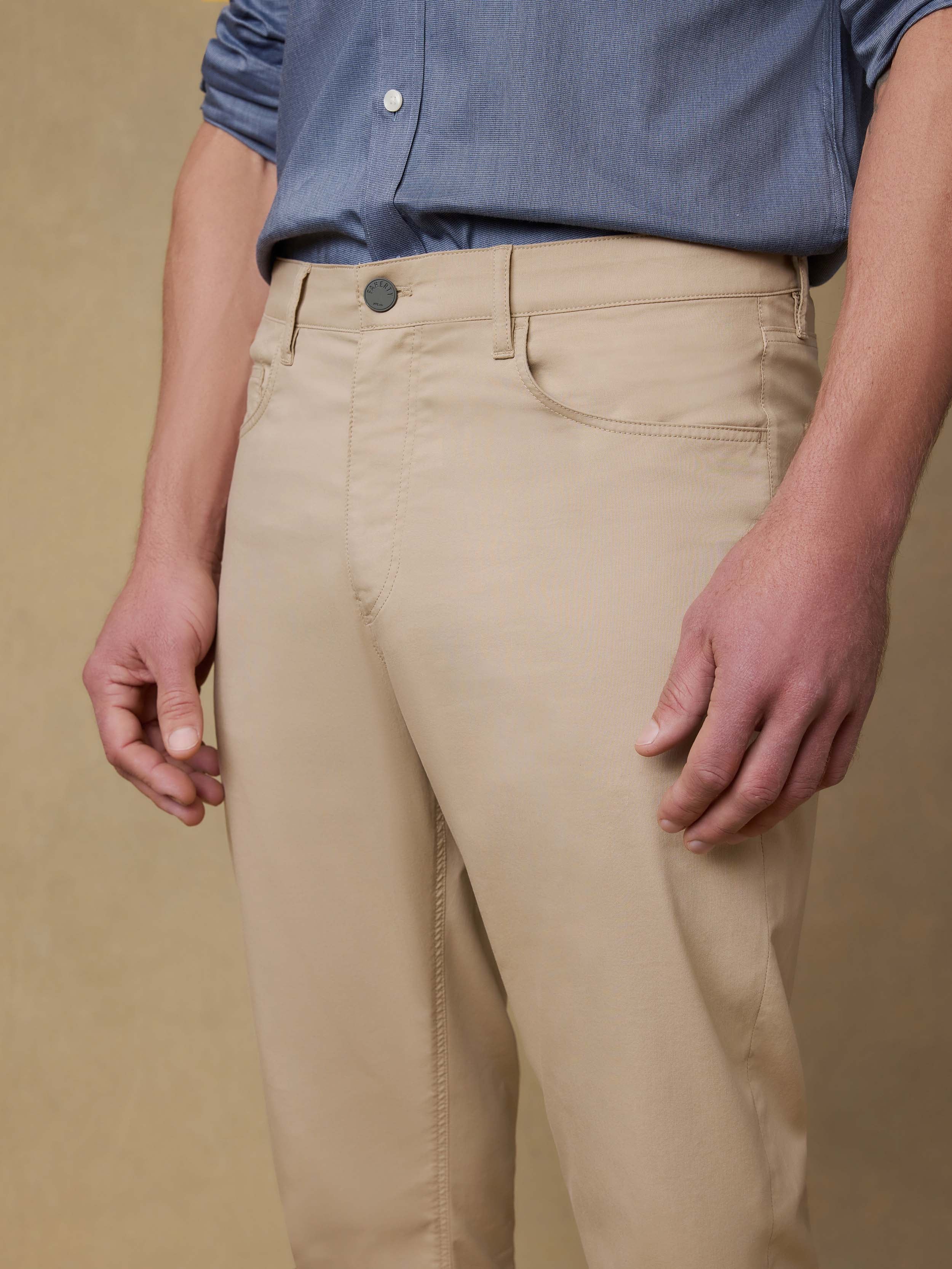 Detail front view of a man wearing a blue button down shirt with beige pants against a beige background