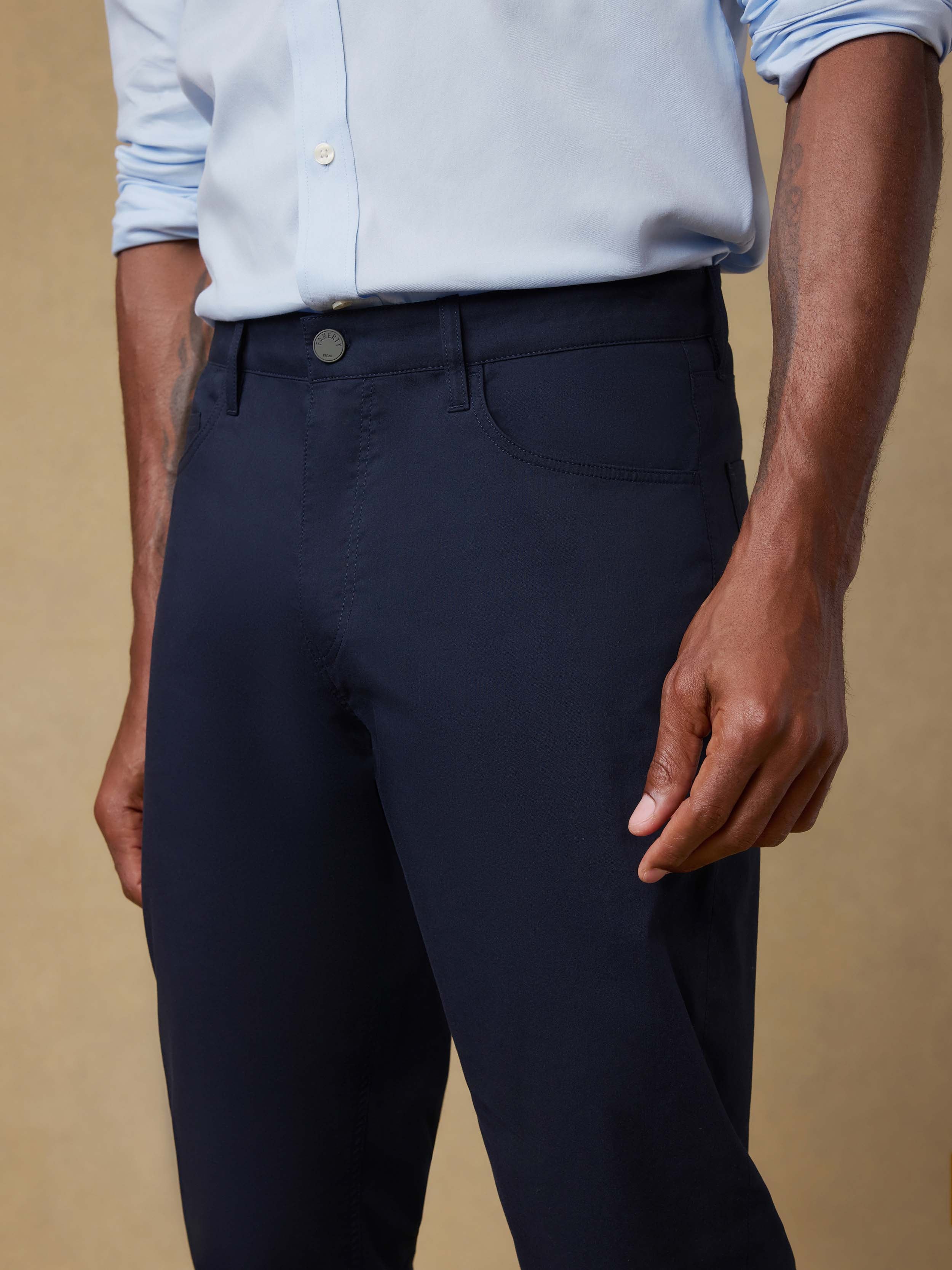 Detail front view wearing a light blue shirt and navy pants against a beige background