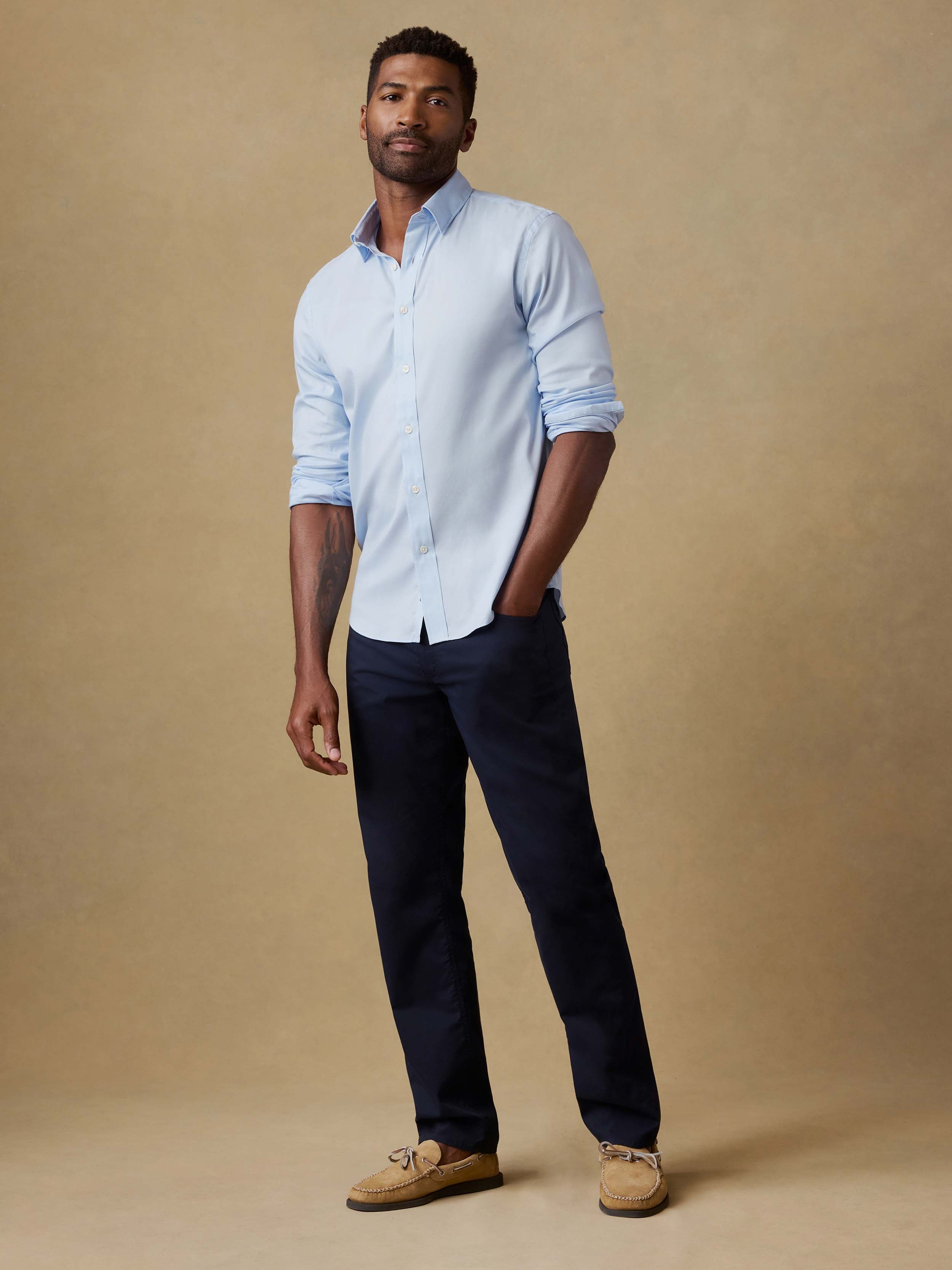 Man wearing a light blue shirt and navy pants against a beige background