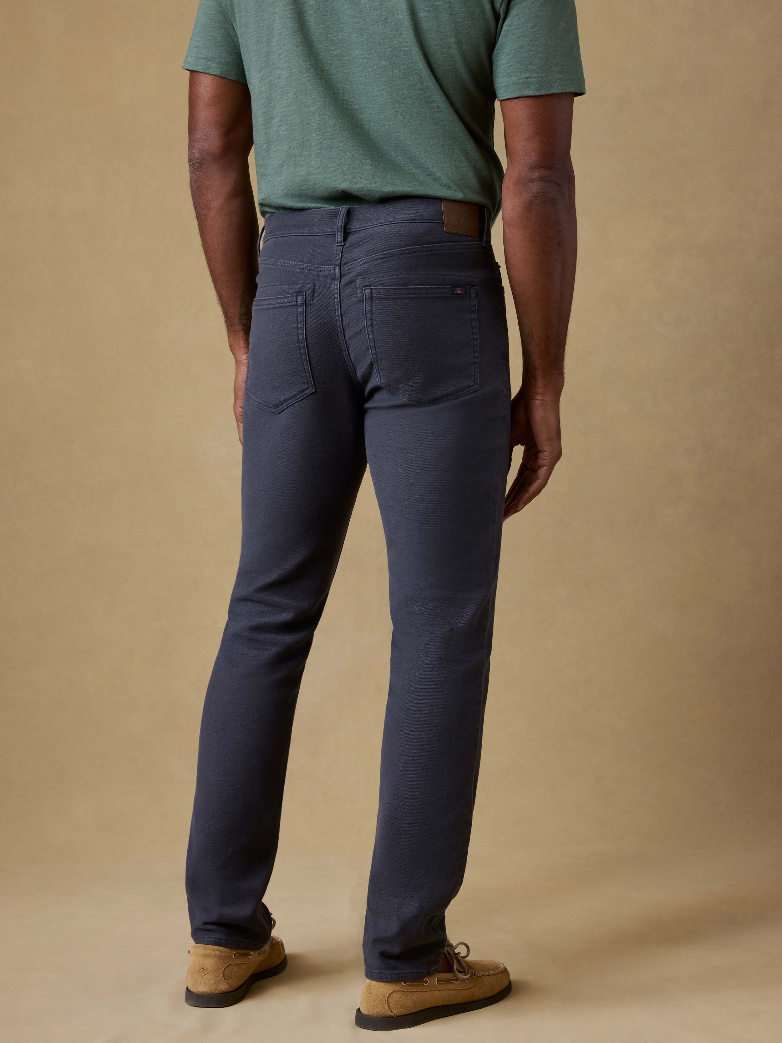 Back view of a man wearing a green t-shirt and navy pants against a beige background