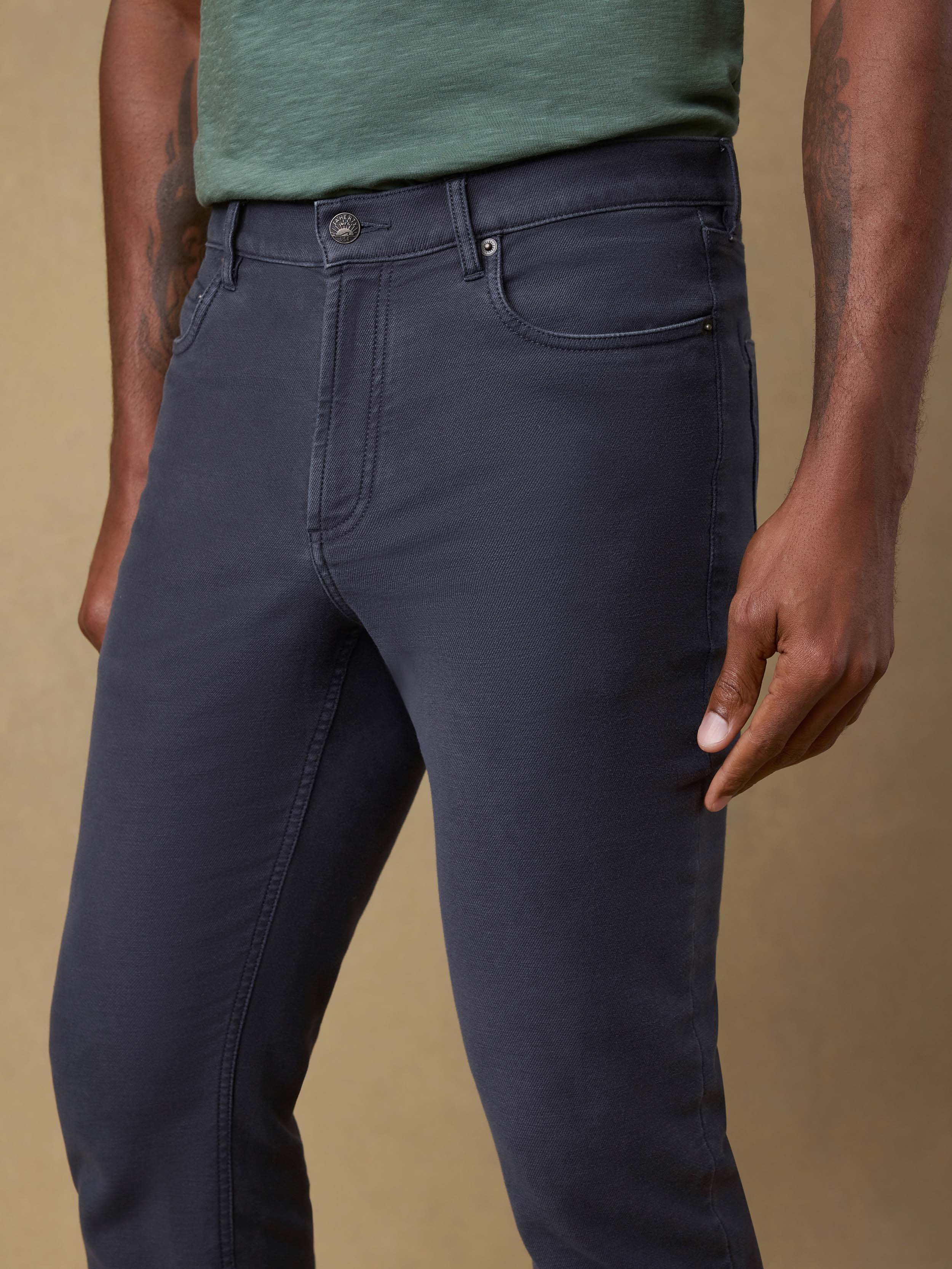 Detail front view of a man wearing a green t-shirt and navy pants against a beige background