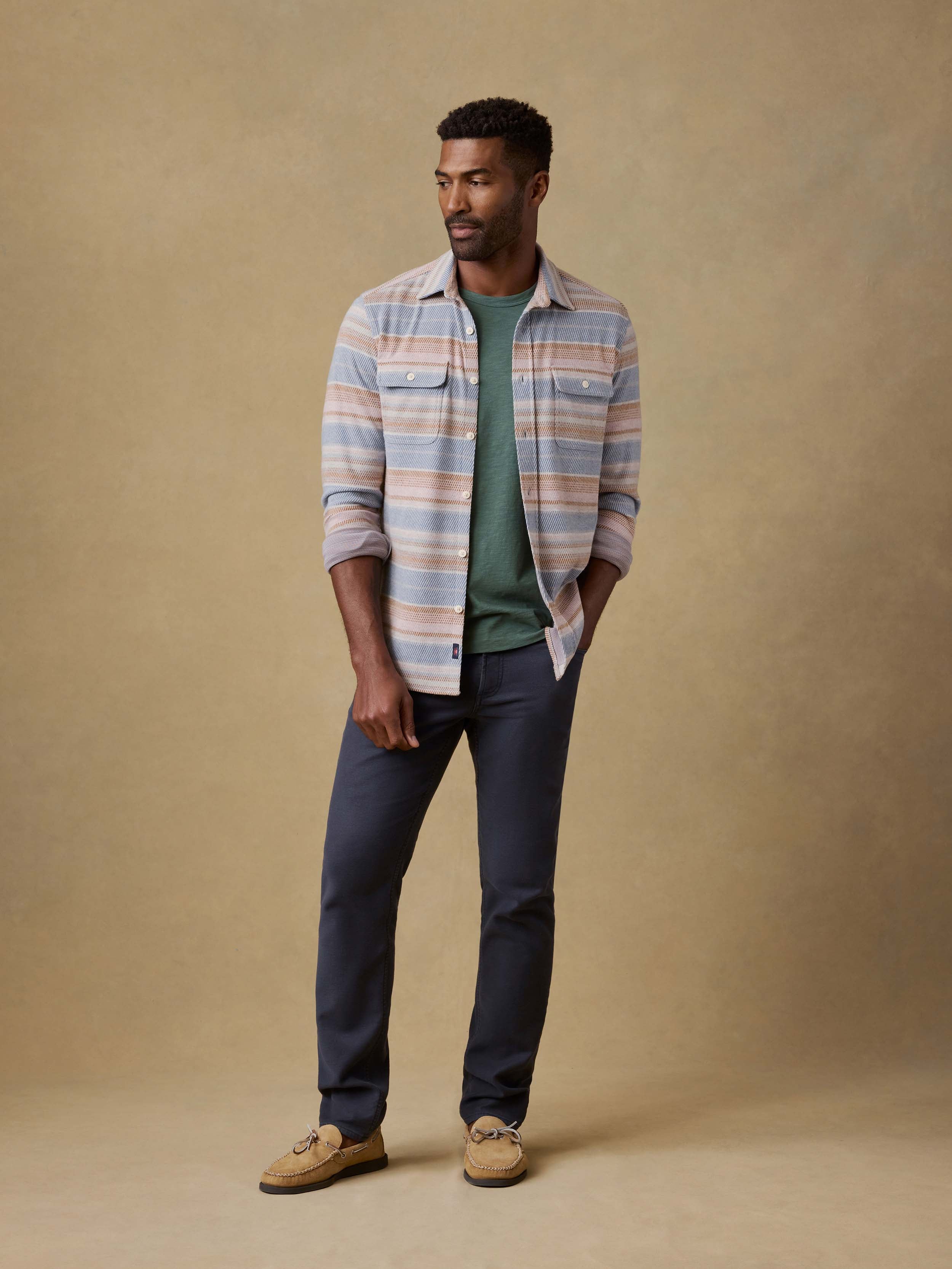 Man wearing a green t-shirt and navy pants against a beige background