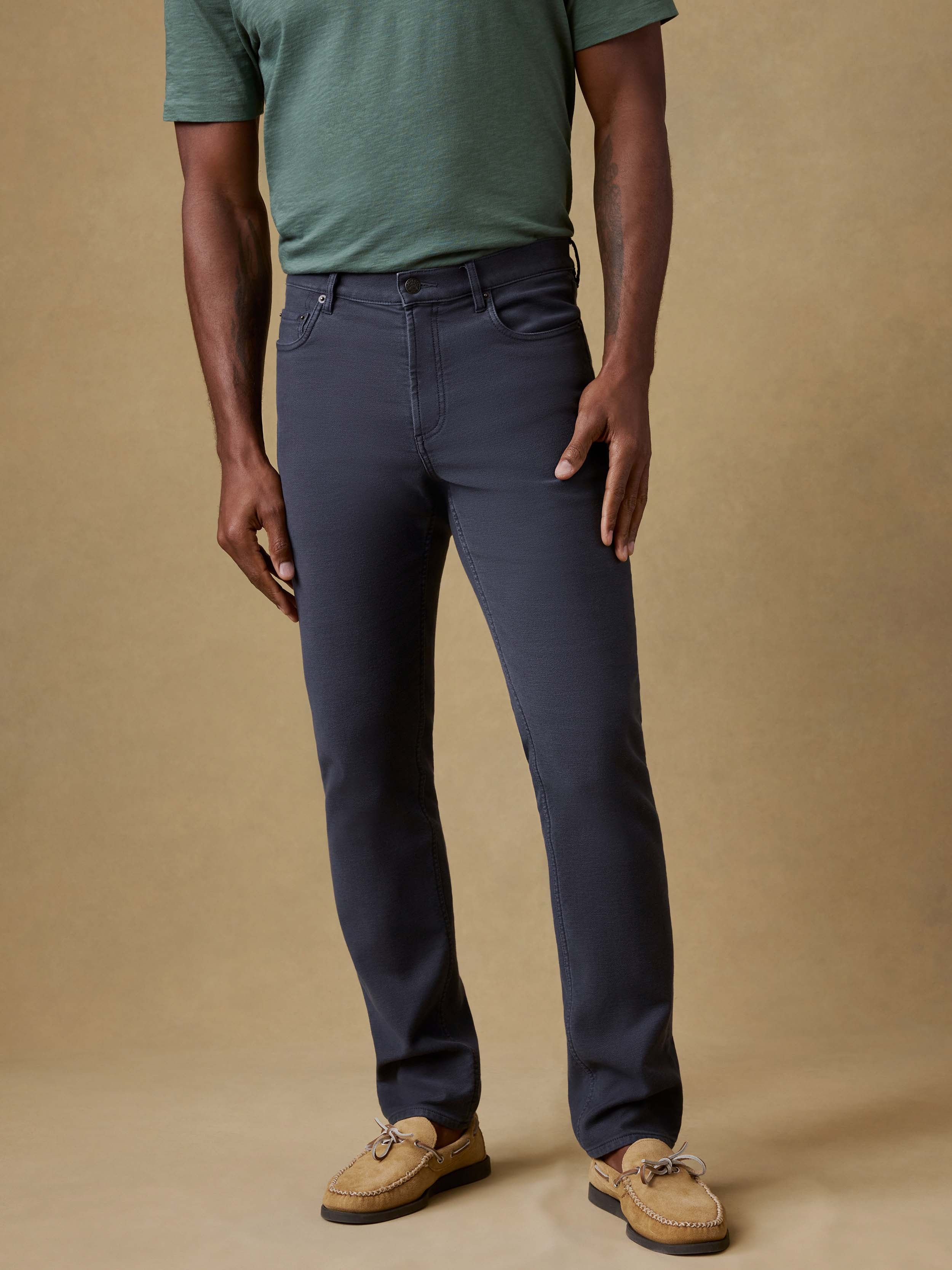 Man wearing a green t-shirt and navy pants against a beige background