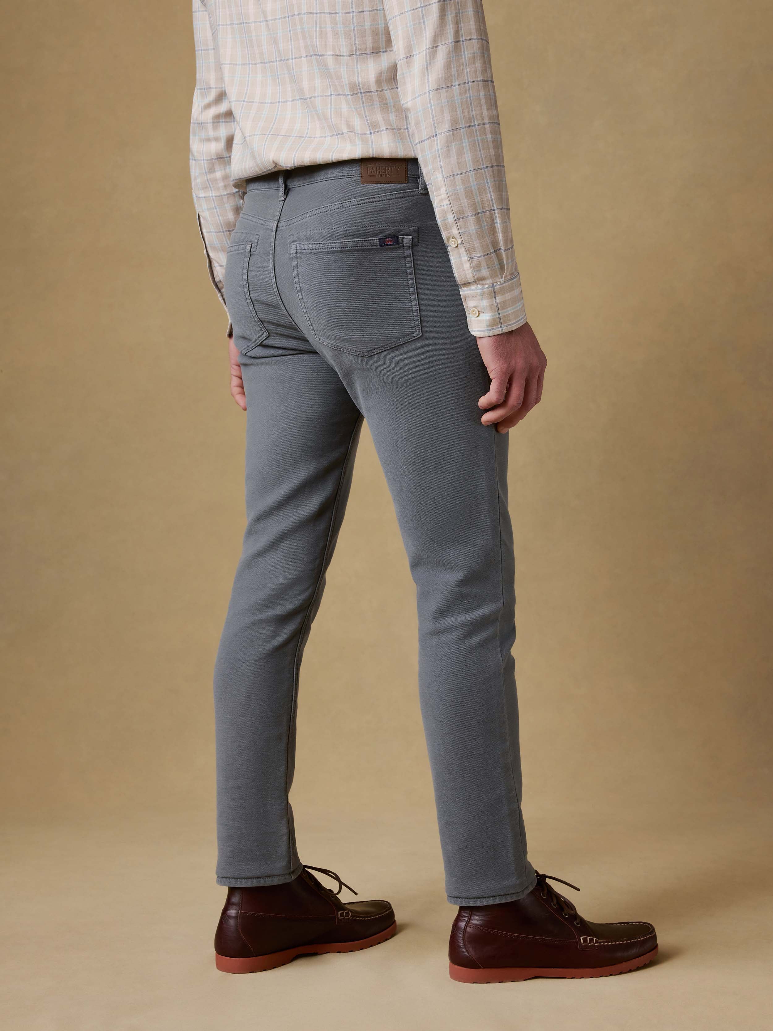 Back view of a man wearing a plaid button down shirt and gray pants against a beige background